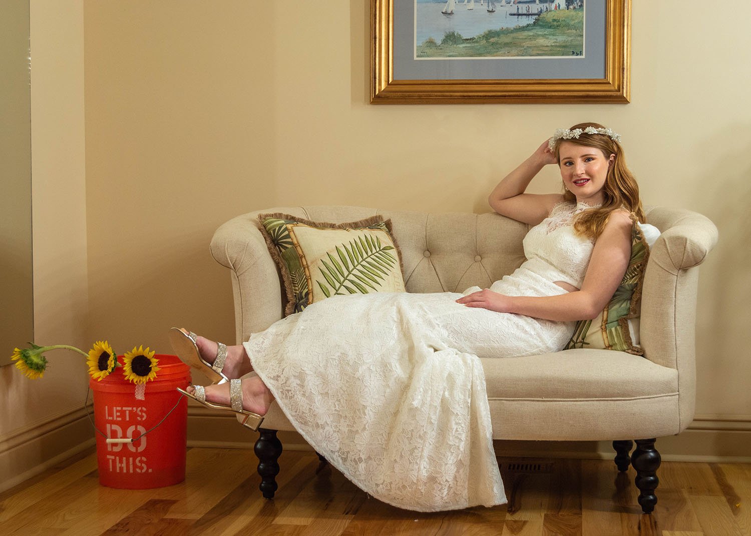 An LGBTQ+ marrier lays across a couch in the getting ready suite at Davidson Farm for a photo. To the their left is a vibrant orange bucket with sunflowers.