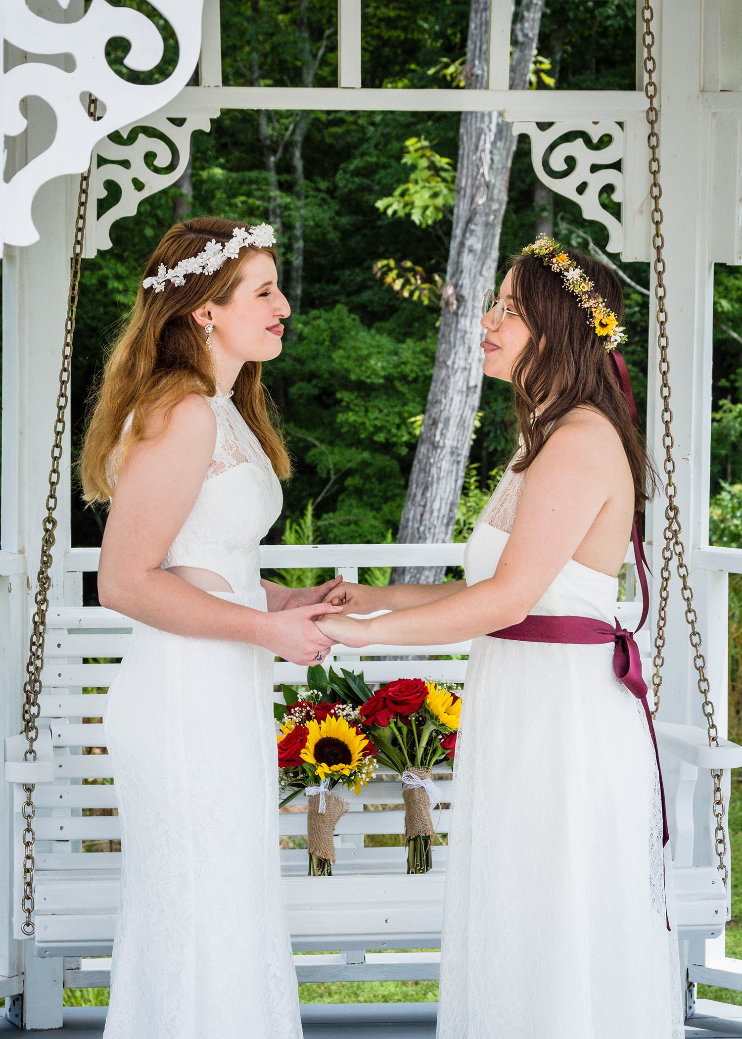 Two LGBTQ+ brides stand holding onto one another as they stick their tongues out for a silly photo.