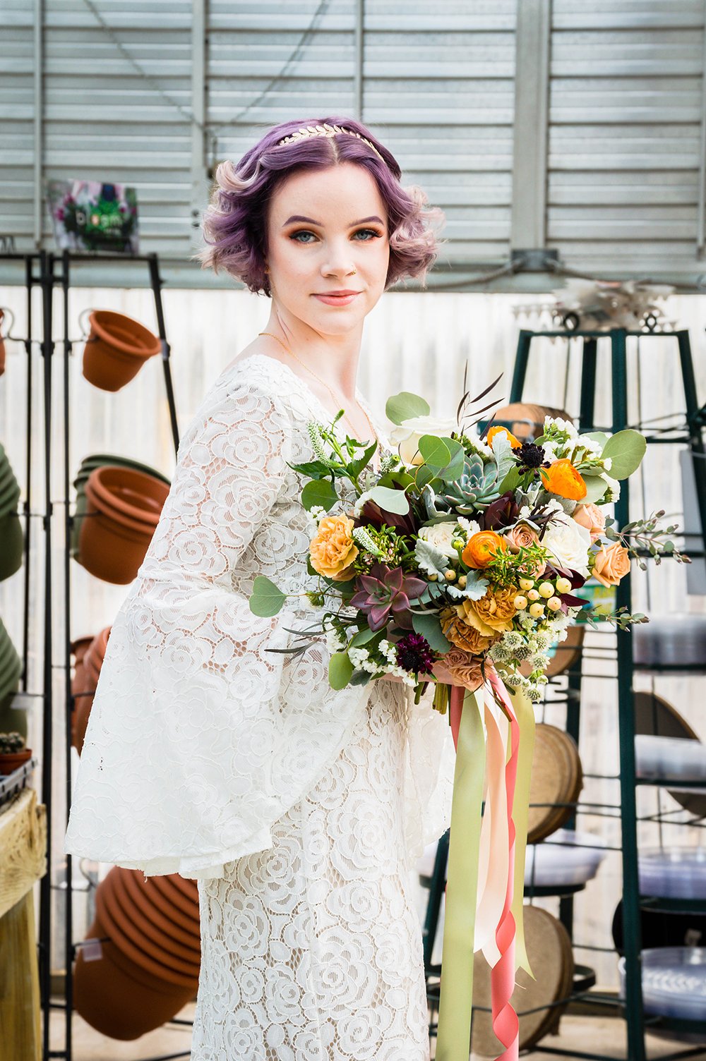 A non-binary lesbian newlywed spouse holds their bouquet inside Greenbrier Nurseries and smiles for a photo.