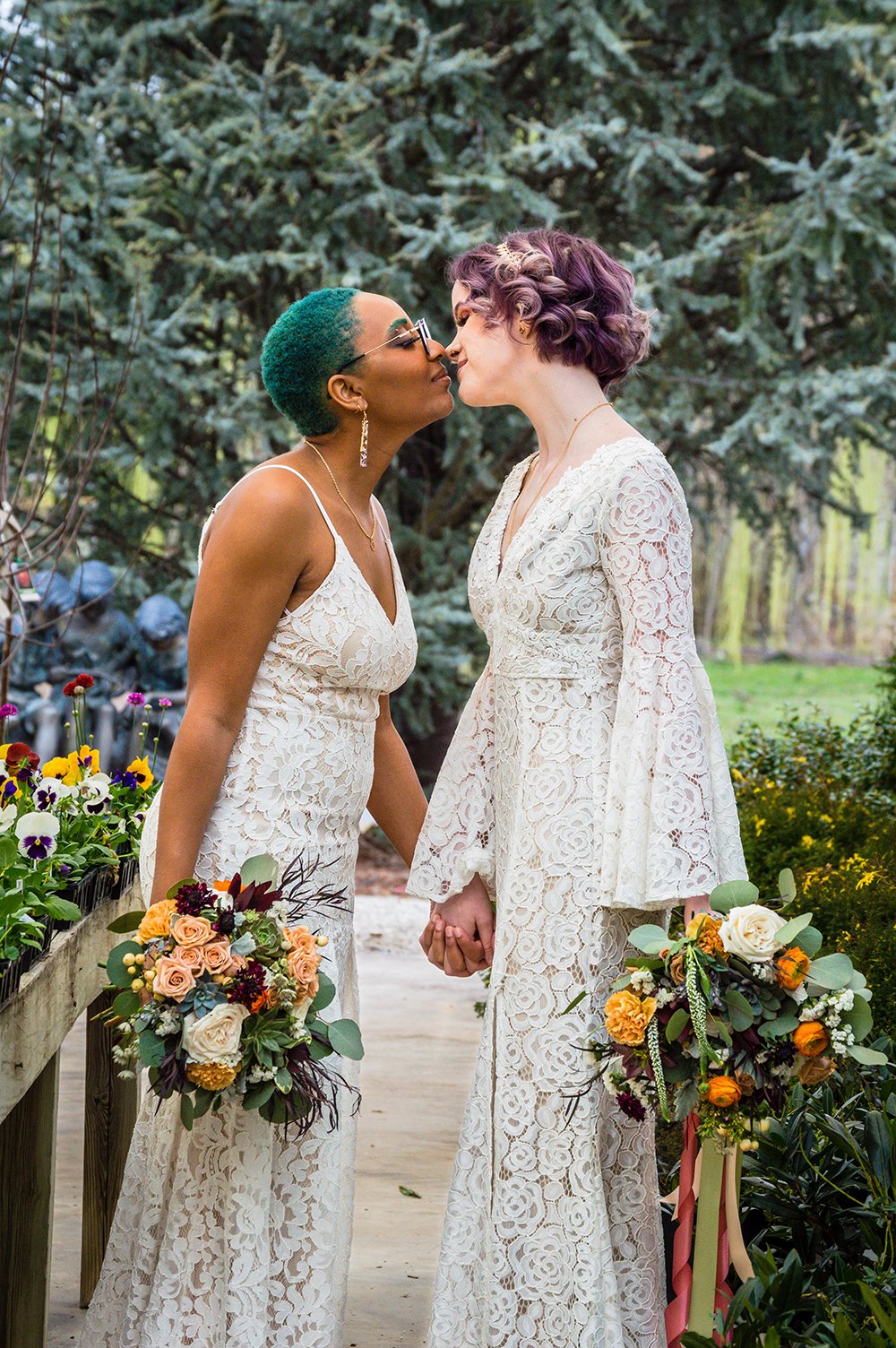 Two non-binary lesbian marriers hold their bouquets to their side as they go in for their first kiss during their elopement.