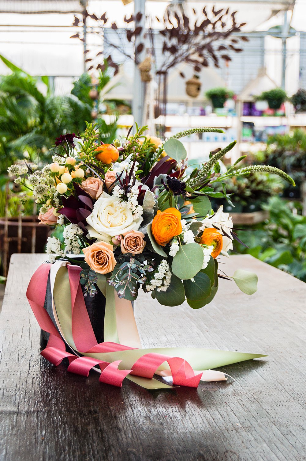 A wedding bouquet with beautiful bright flowers and green succulents wrapped in long pink, green, and cream ribbon sits inside a pot at Greenbrier Nurseries.