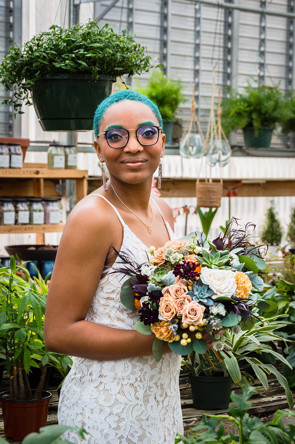 A non-binary lesbian newlywed spouse holds their bouquet inside Greenbrier Nurseries and smiles for a photo.