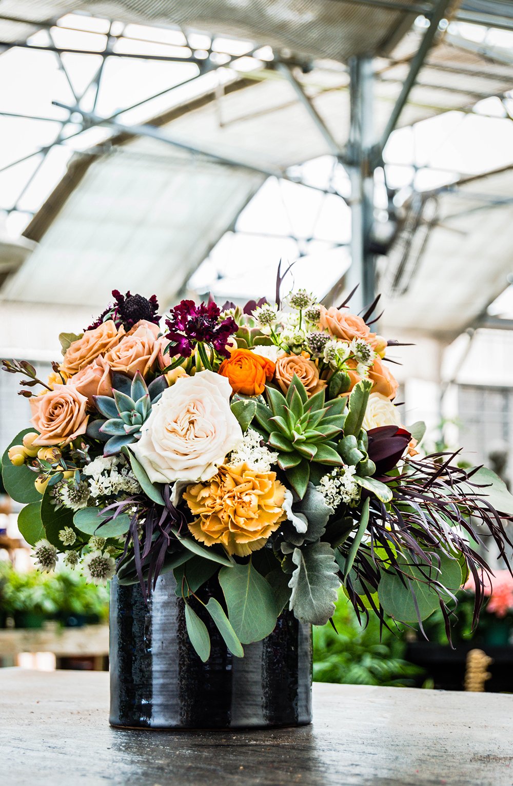 A vibrant wedding bouquet of flowers with succulents and roses inside a black pot at Greenbrier Nurseries.