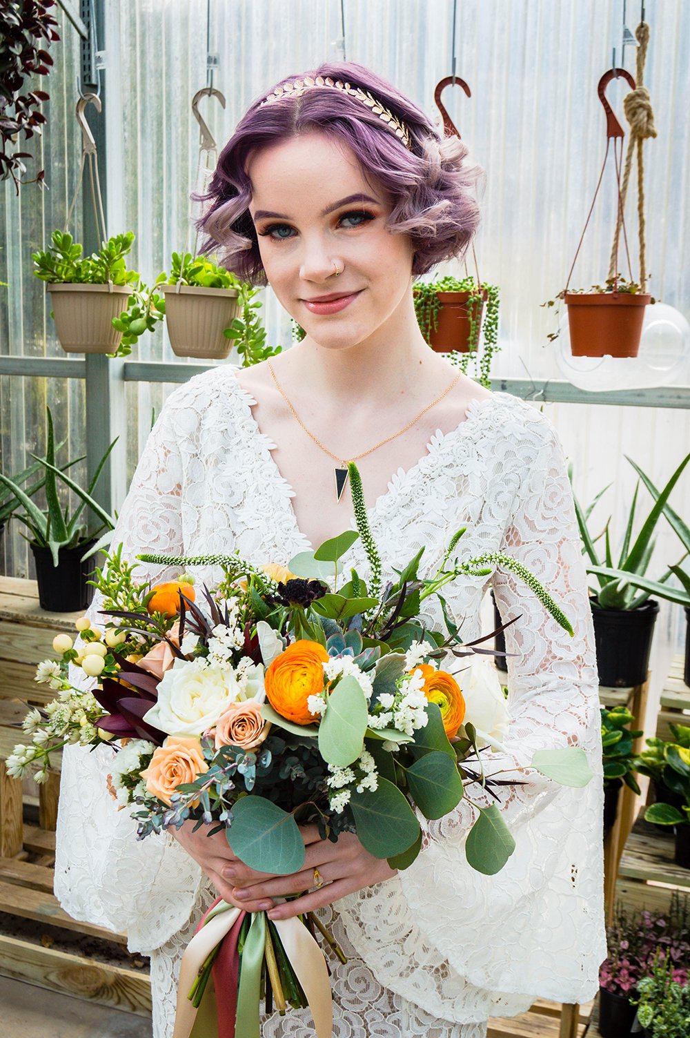 A queer newlywed spouse holds their bouquet inside Greenbrier Nurseries and smiles for a photo.