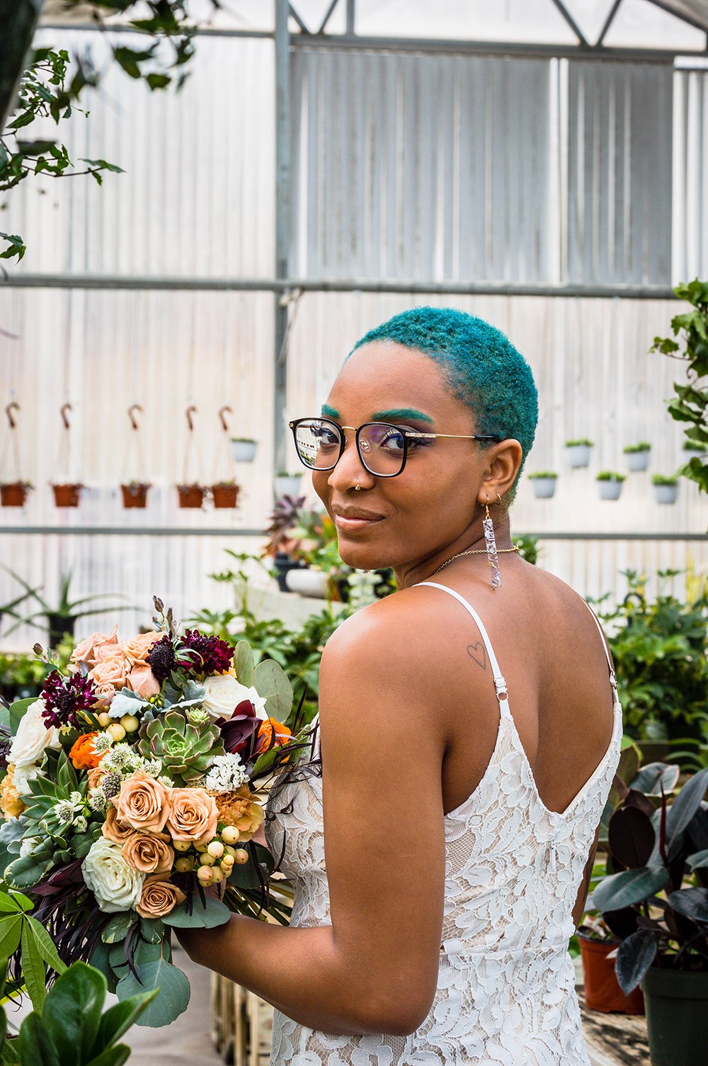 A non-binary lesbian newlywed spouse holds their bouquet inside Greenbrier Nurseries and smiles for a photo.