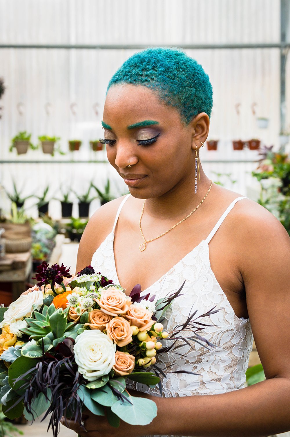 An lgbtq+ spouse holds their wedding bouquet inside Greenbrier Nurseries and closes their eyes to show off their makeup.