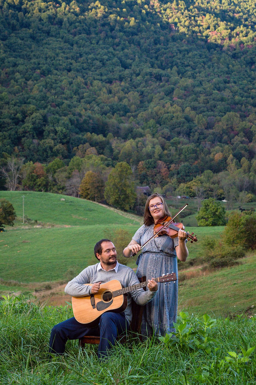 A couple plays a violin and guitar atop of a hill overlooking the Blue Ridge Mountains.