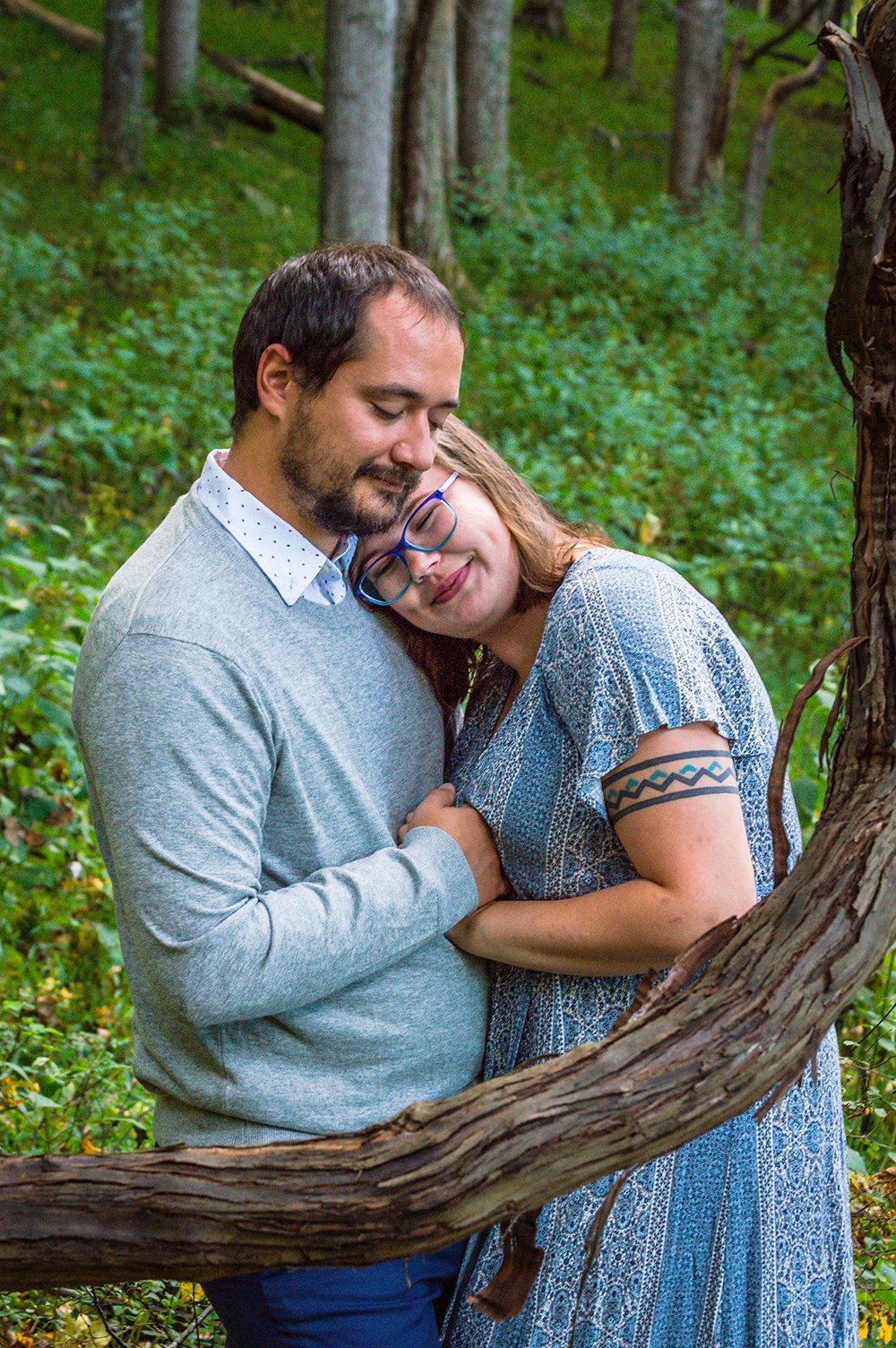 A couple embraces behind a bent branch on the bottom of a forested hill during their adventure couple’ session in Blacksburg, Virginia.