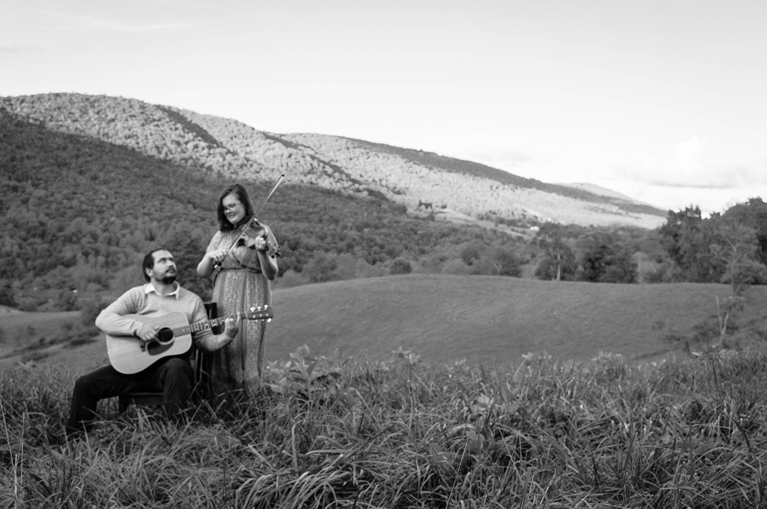 A couple plays a violin and guitar atop of a hill overlooking the Blue Ridge Mountains.