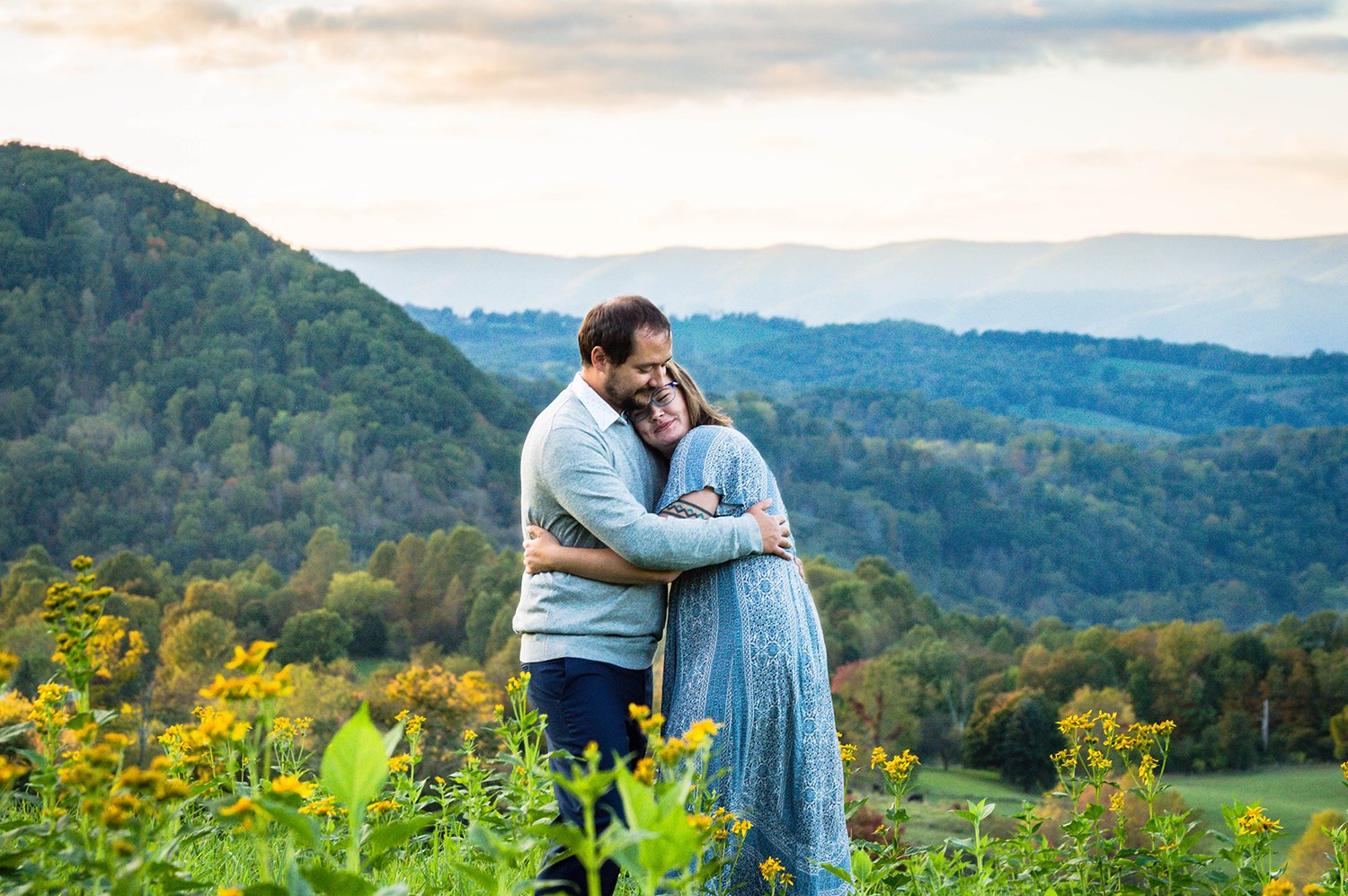 A couple embraces atop of a hill overlooking the Blue Ridge Mountains.