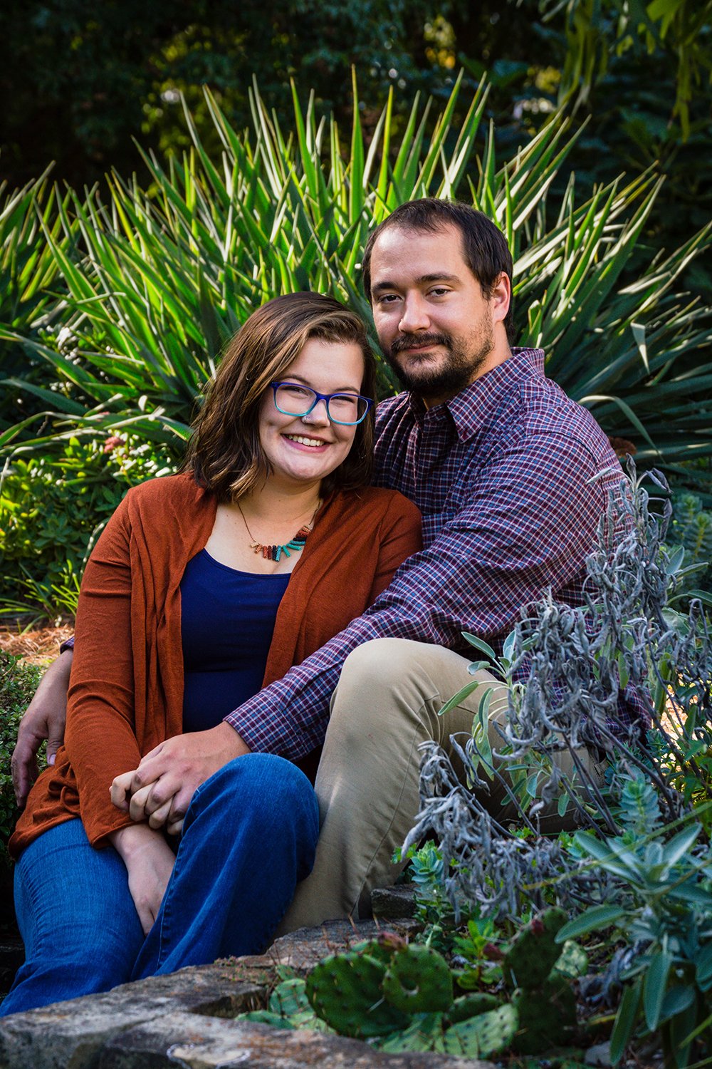 A couple sits on steps surrounded by various plants in a garden on Virginia Tech's campus for a couple's adventure session in Blacksburg, Virginia.