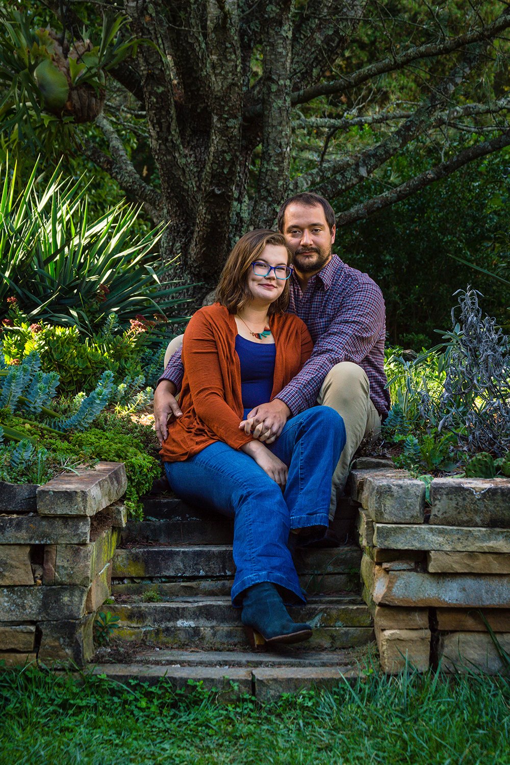 A couple sits on steps surrounded by various plants in the Hahn Horticulture Garden on Virginia Tech's main campus for a couple's adventure session in Blacksburg, Virginia.