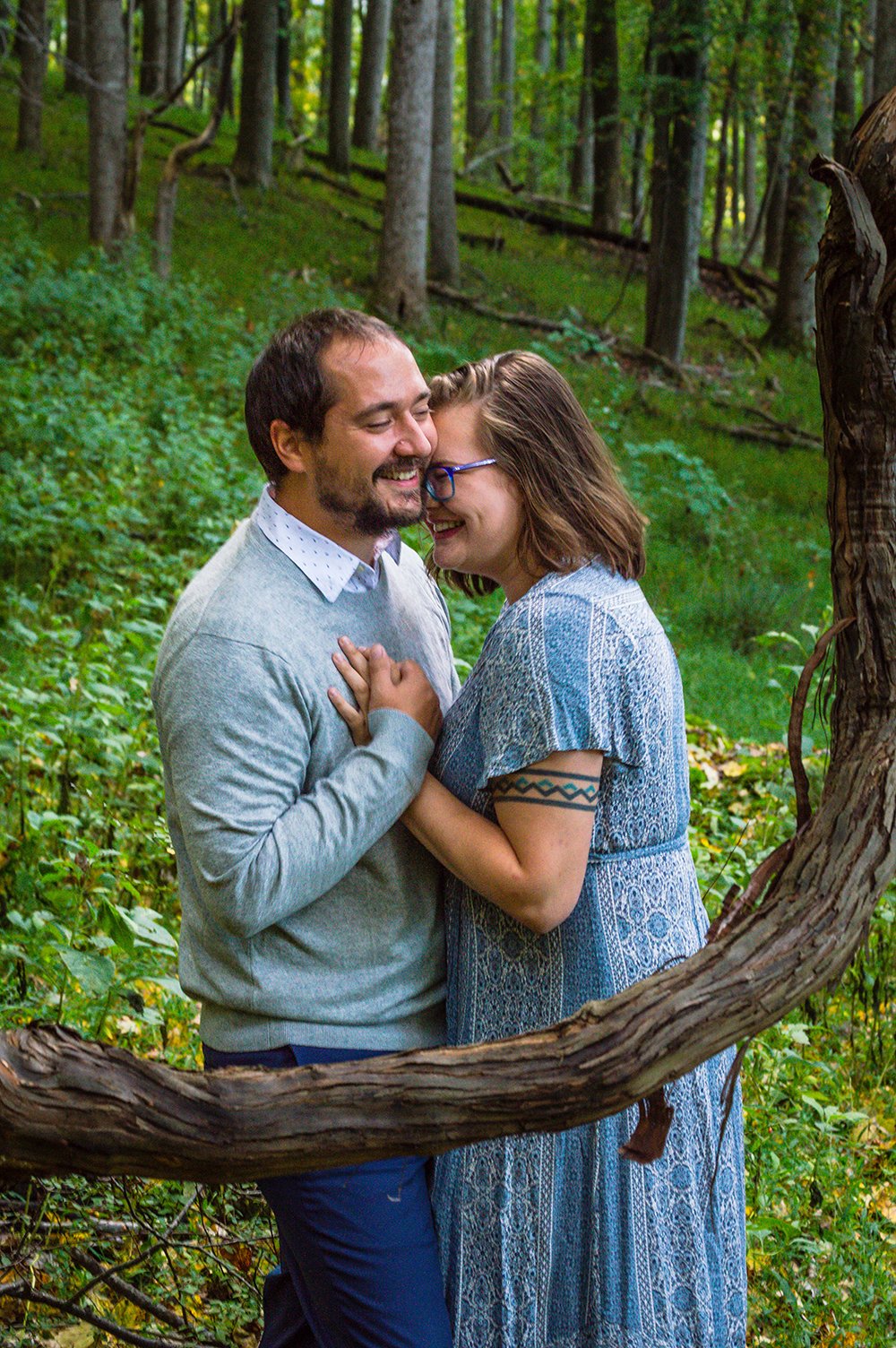 A couple embraces behind a bent branch on the bottom of a forested hill during their adventure couple’ session in Blacksburg, Virginia.