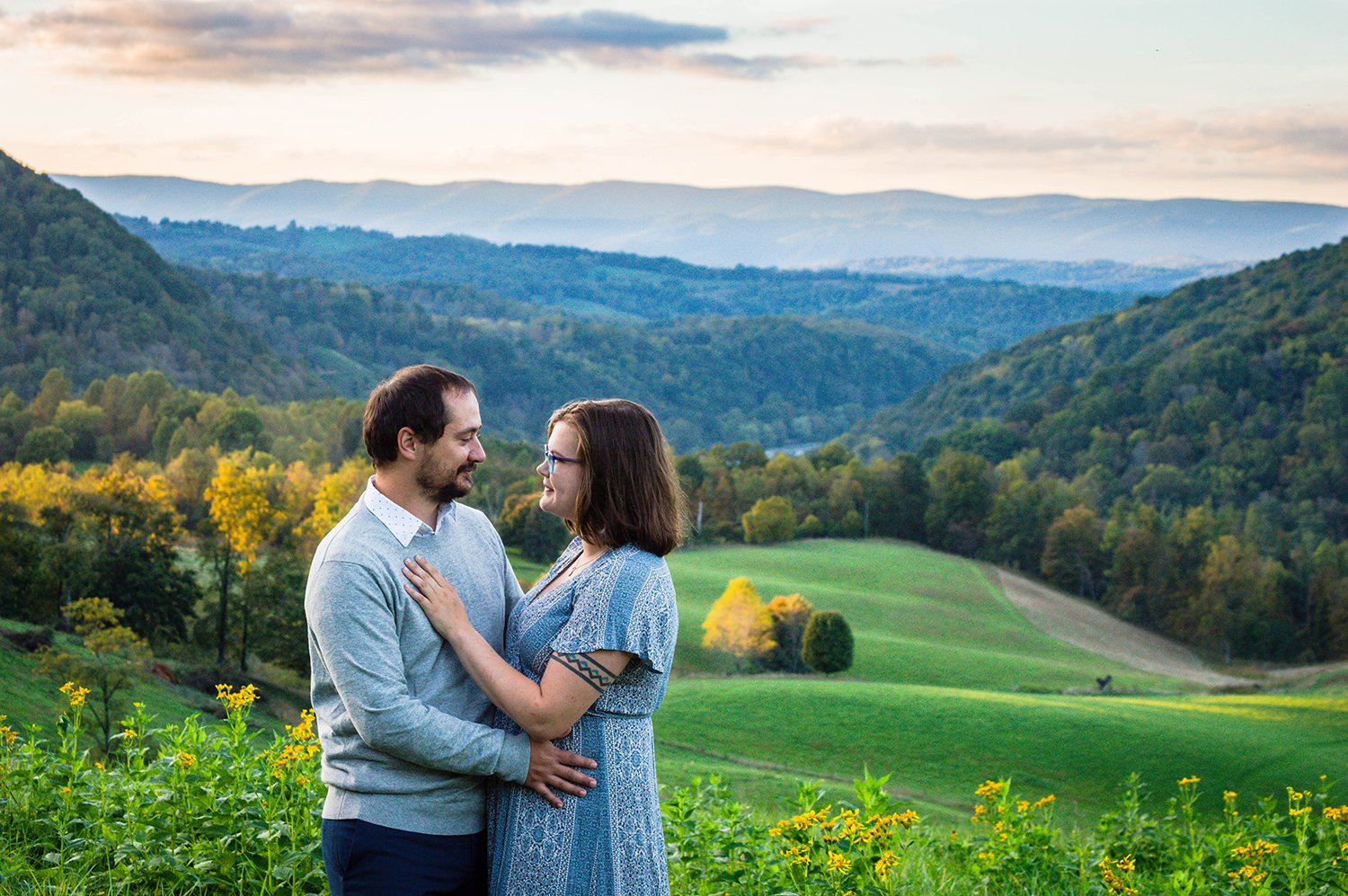 A couple embraces atop of a hill overlooking the Blue Ridge Mountains for a couple's adventure session in Blacksburg, Virginia.