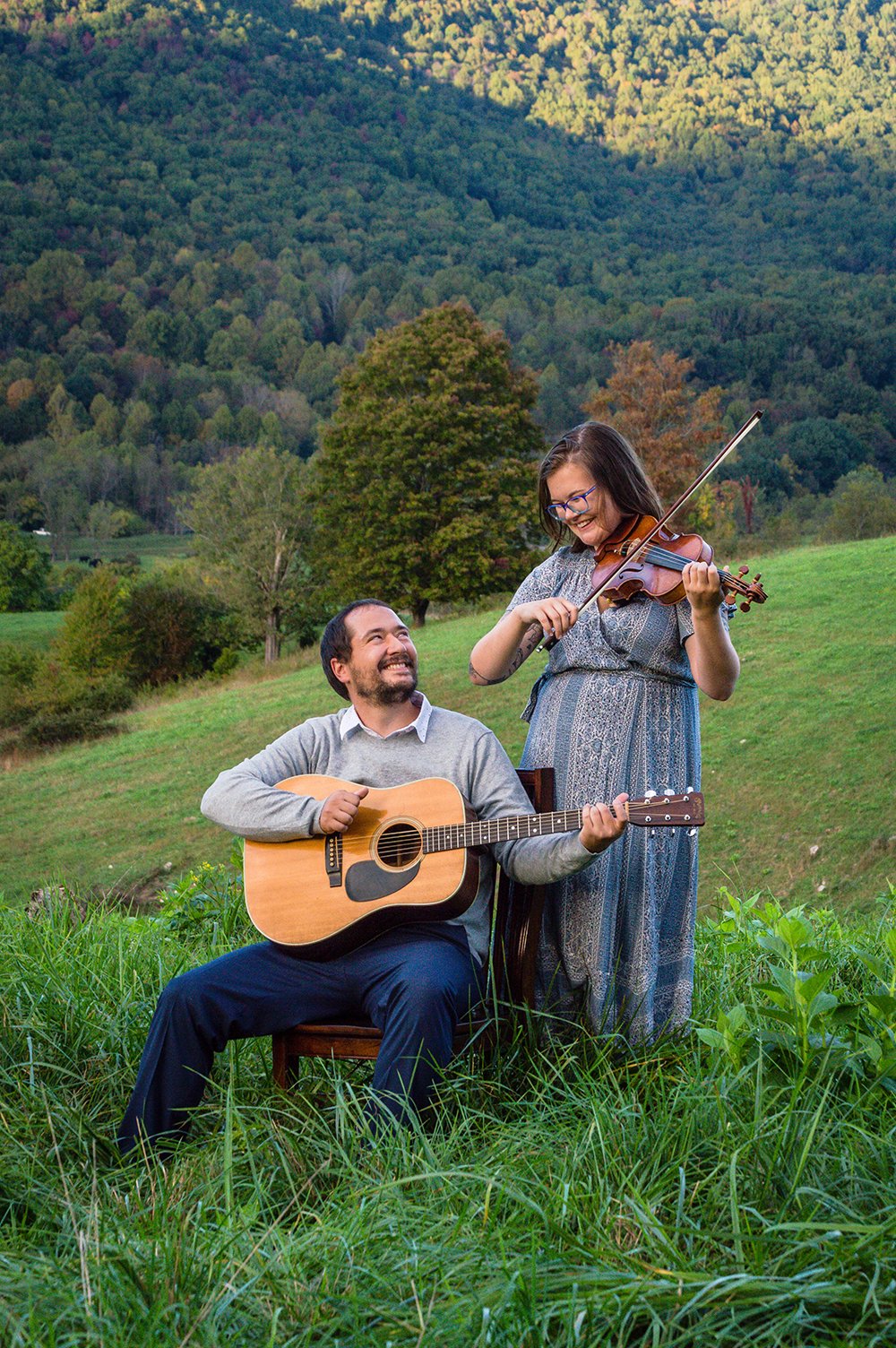 A couple plays a violin and guitar atop of a hill overlooking the Blue Ridge Mountains.