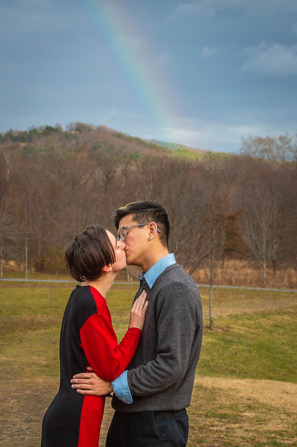 A couple kisses as a rainbow appears in the sky.