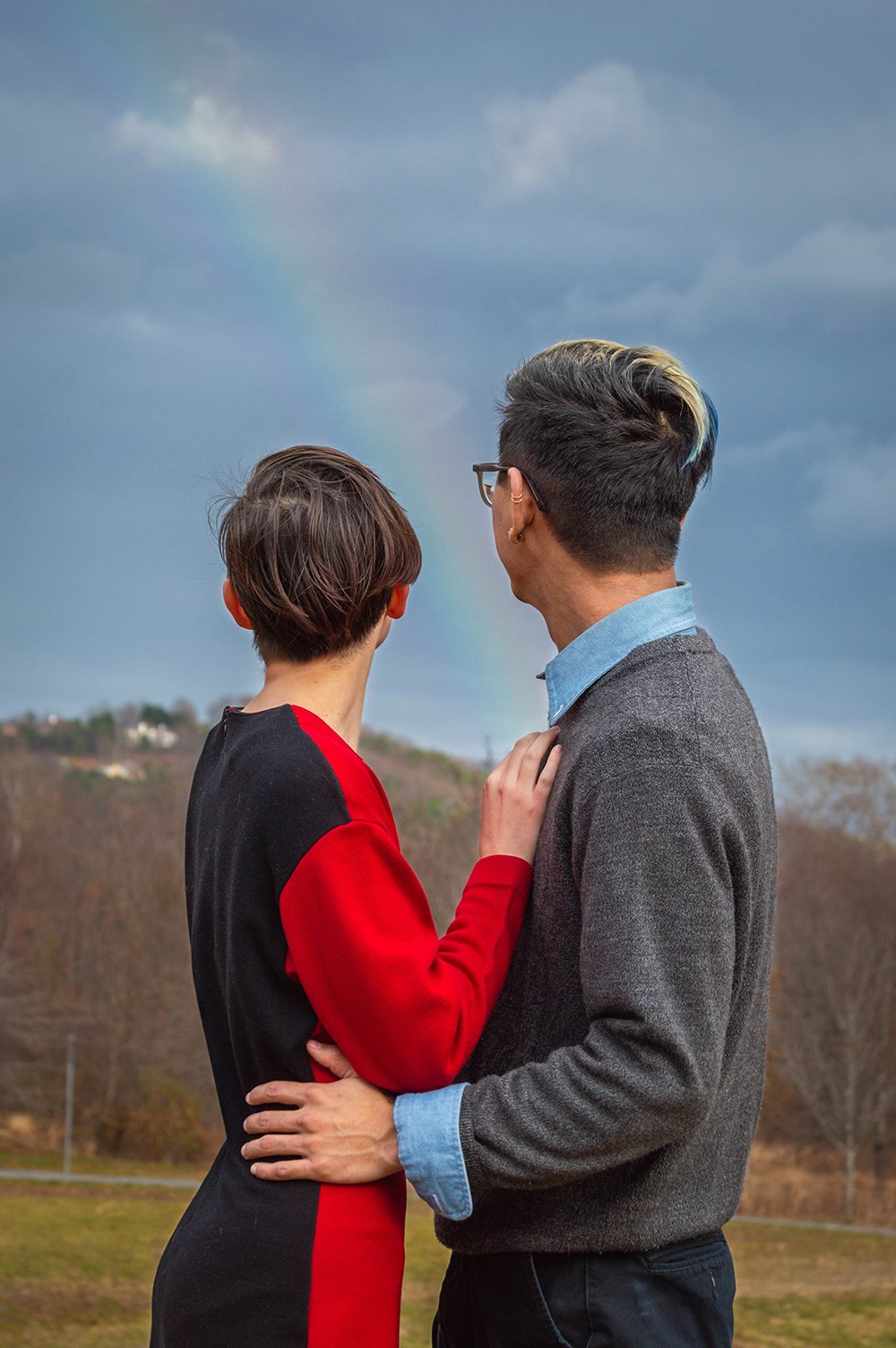 A couple embraces as they look away from the camera briefly to see a rainbow that appeared.