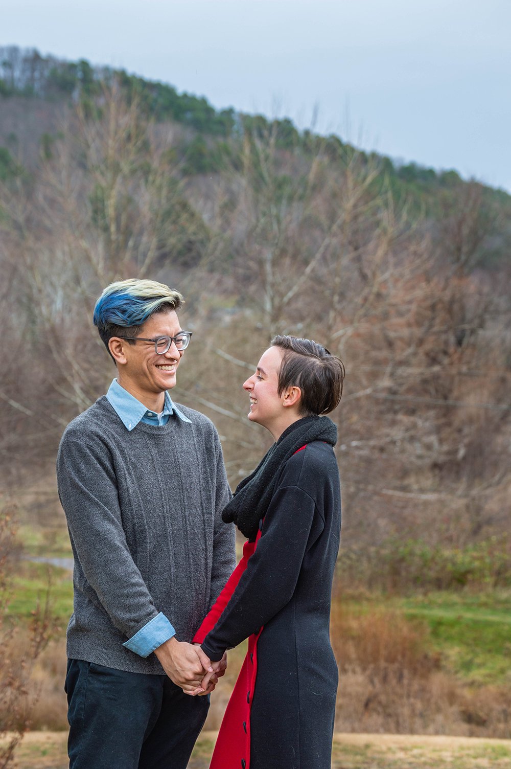 A couple holds hands and stands in front of one another smiling during their adventure couple’s session in Roanoke, Virginia at the South County Public Library.