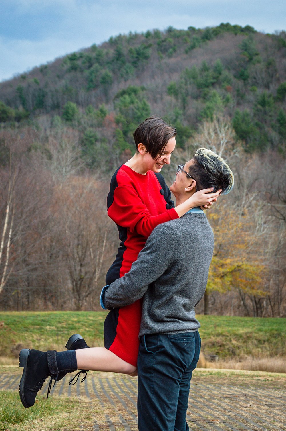 A man lifts a woman in the air and the woman smiles towards the man during an adventure couple’s session in Roanoke, Virginia.