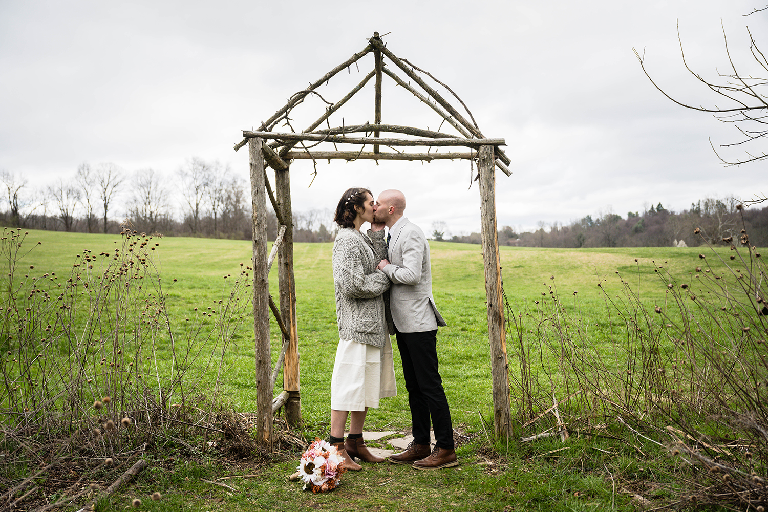 A couple on their elopement day embraces and has their first kiss at under a altar made of sticks at Heritage Park in Blacskburg, Virginia.