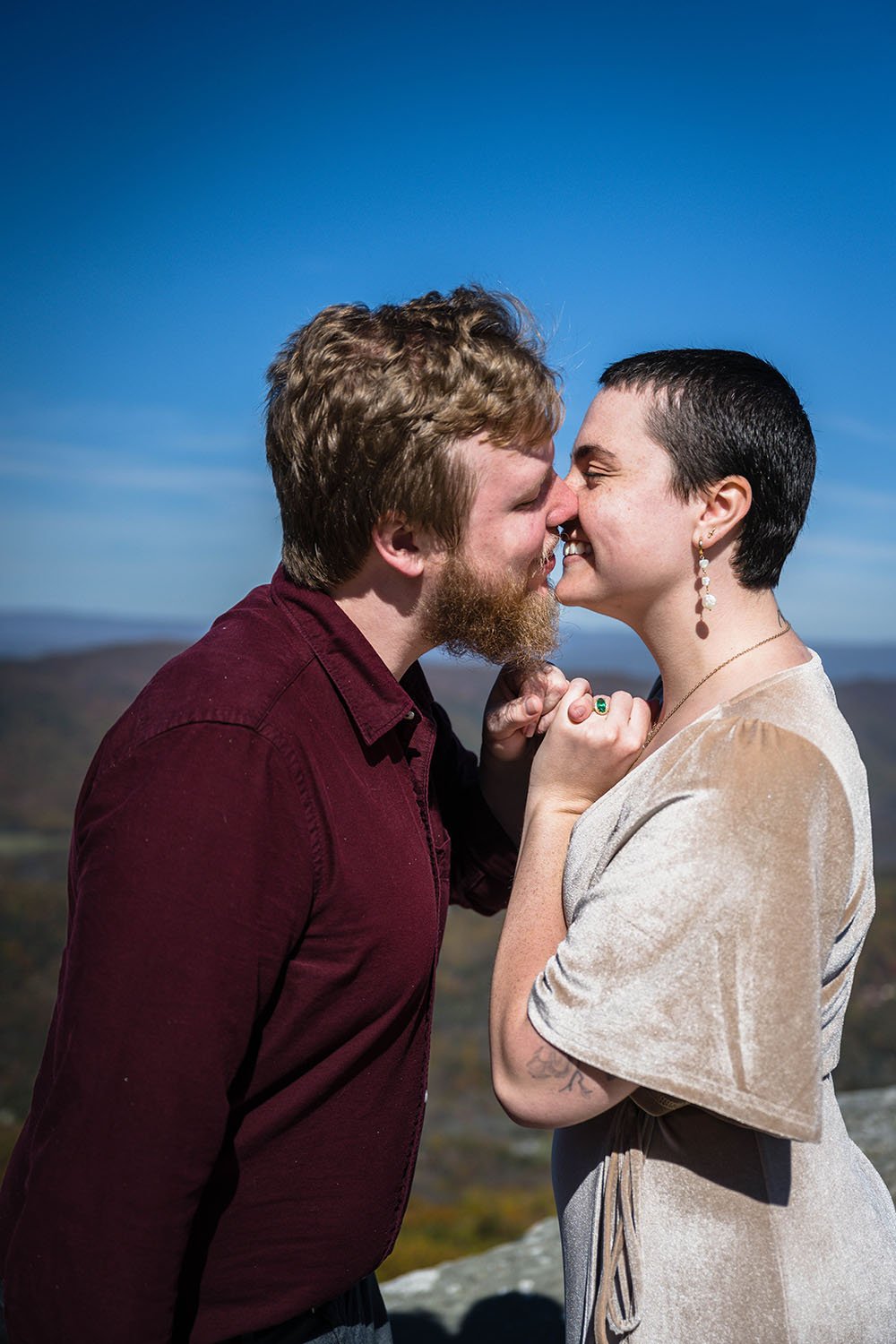 A couple intertwines their pinkies and go in for a kiss on the summit of McAfee Knob during their engagement session.