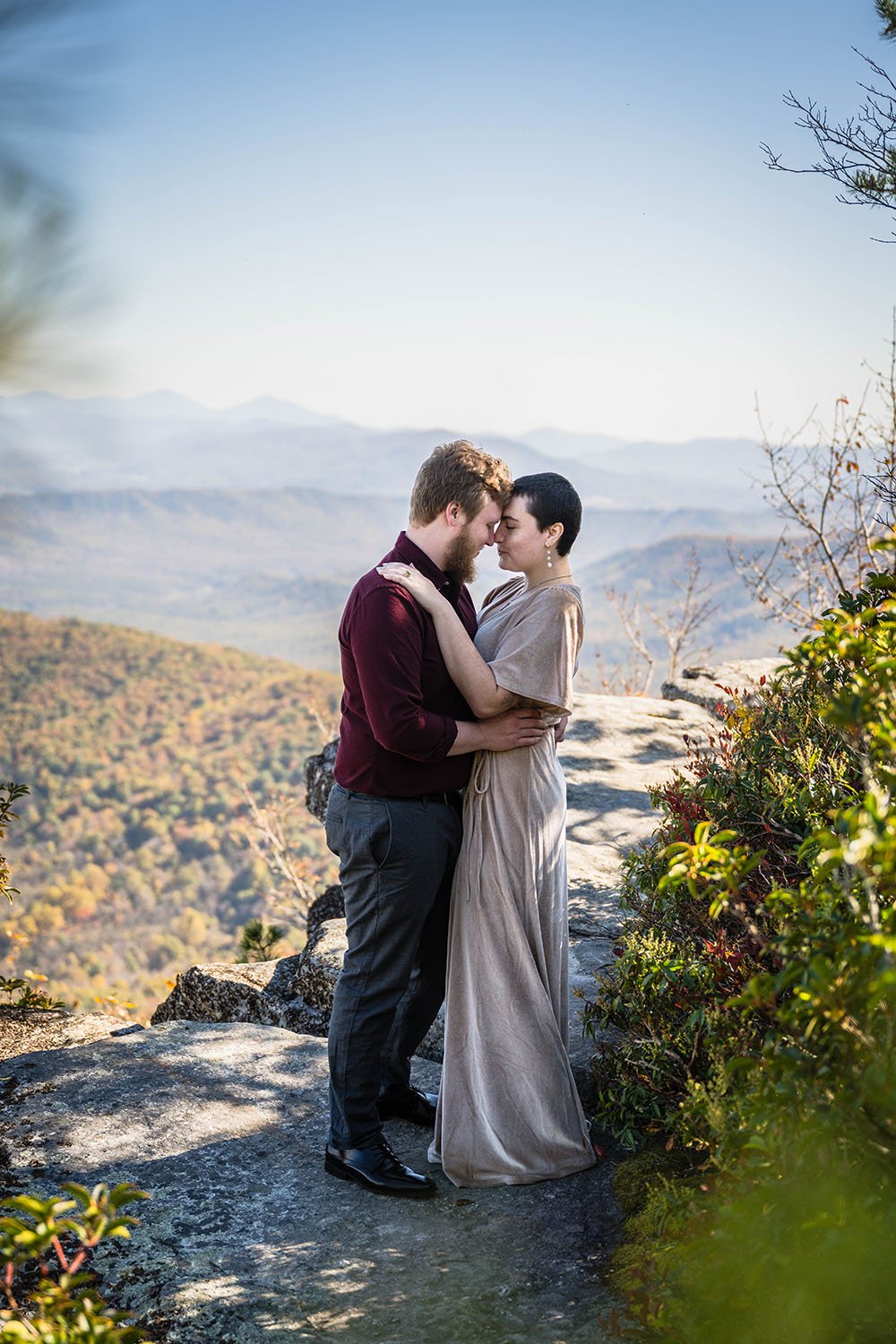 A couple embraces at the summit of McAfee Knob with the Blue Ridge Mountains in the background during their engagement photoshoot.