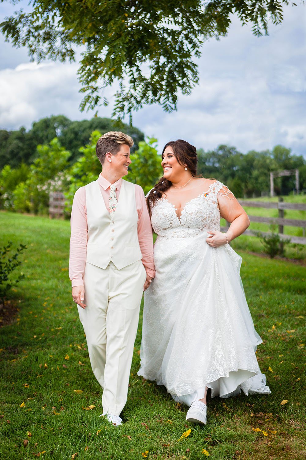 Two LGBTQ+ marriers walk together hand in hand and smile towards one another for a photo during their wedding day at The Pavilion at Black Water Junction in Virginia.