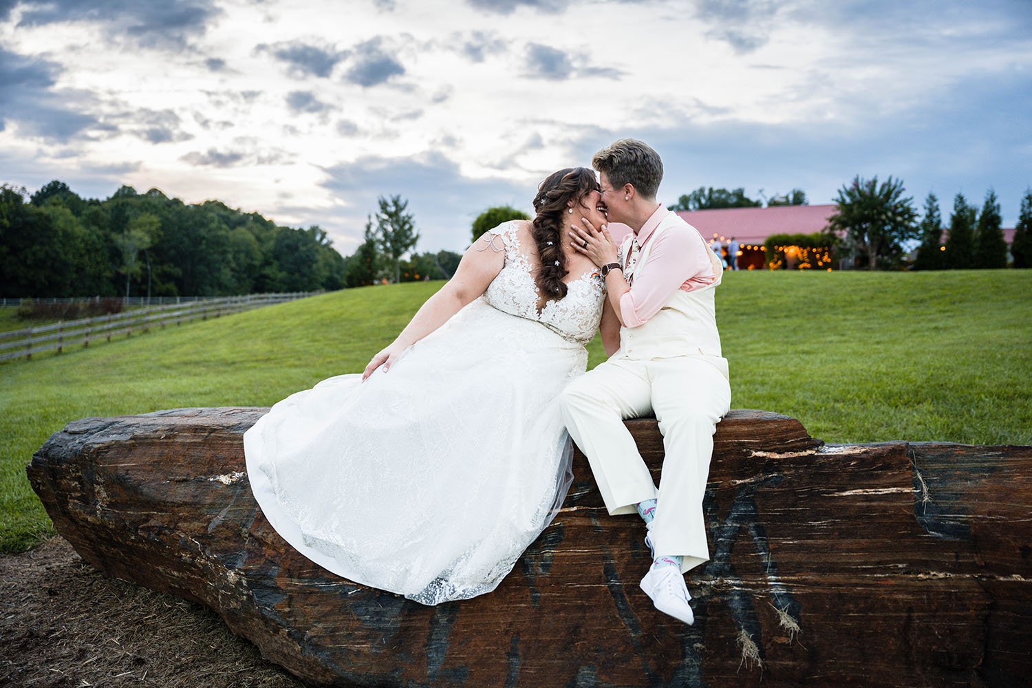 An lgbtq+ wedding couple sit atop of a large rock at the Pavilion at Black Water Junction and kiss one another lovingly.