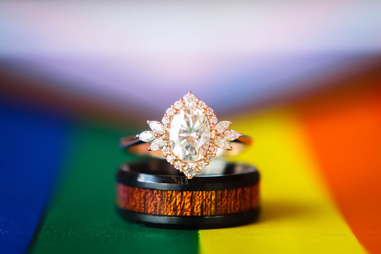 Two wedding rings stacked on top of each other and laying on a rainbow flag.