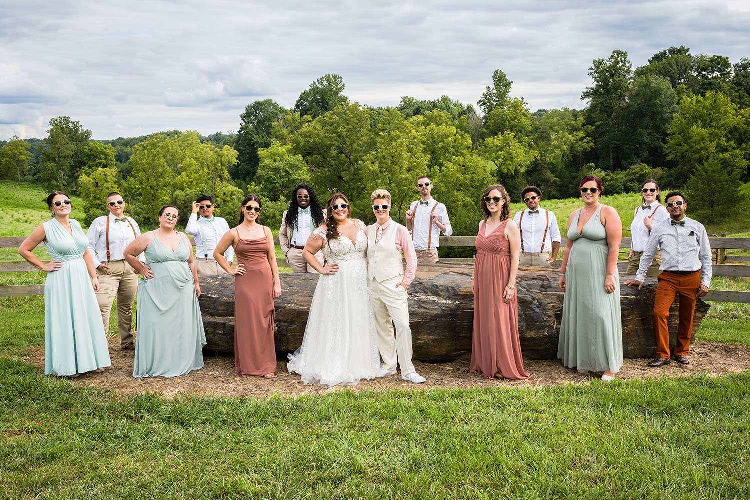 Both wedding parties come together encircling a large rock at the Pavilion at Black Water Junction wedding venue sporting sunglasses.