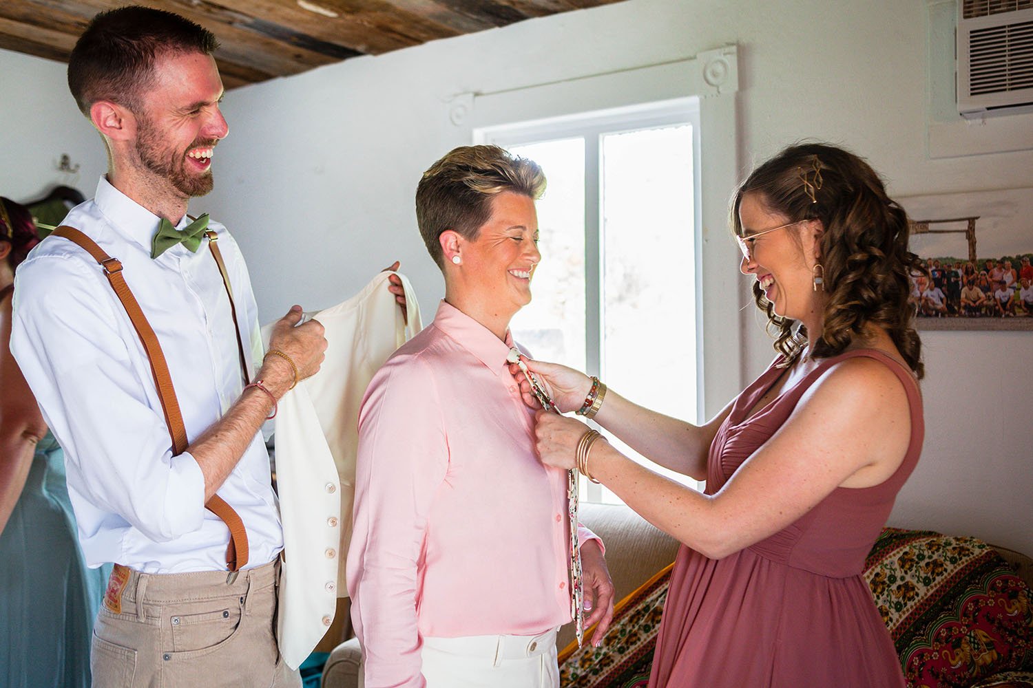 The siblings of the lgbtq+ marrier help put on the marrier's vest and tie in a getting ready suite.