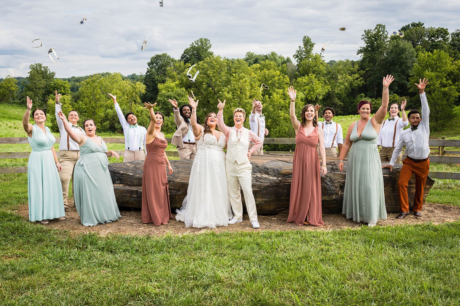 Both wedding parties come together encircling a large rock at the Pavilion at Black Water Junction wedding venue throwing their sunglasses in the air.