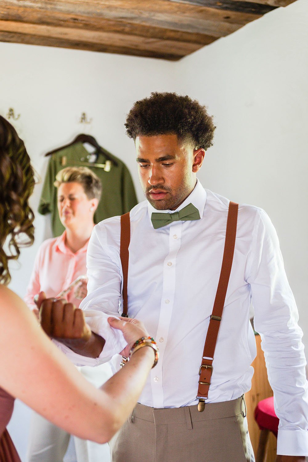 A person off camera helps adjust the sleeves of a member of the wedding party in a getting ready suite.