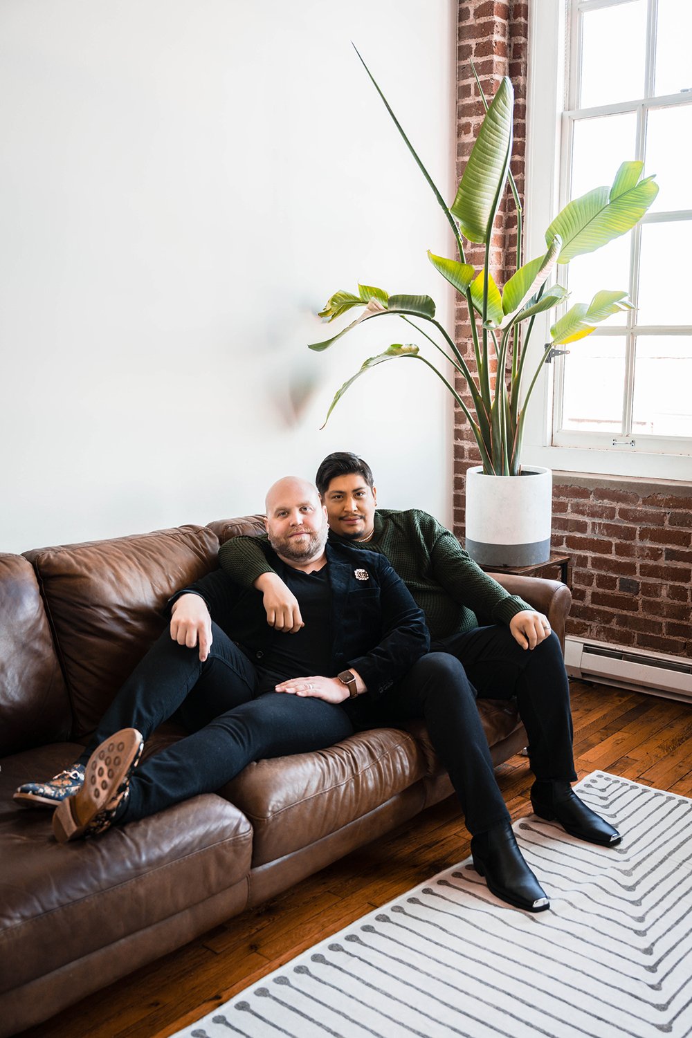 A queer couple sits on the couch in their living room.