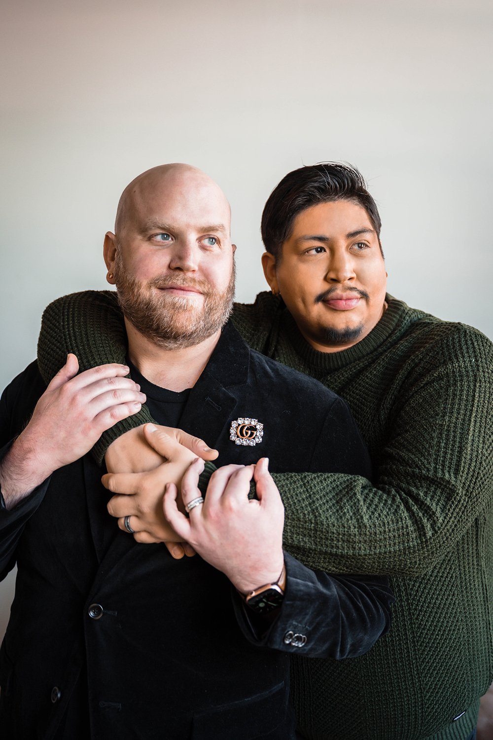 An lgbtq+ couple embraces one another and stare out the window during their at-home photoshoot.