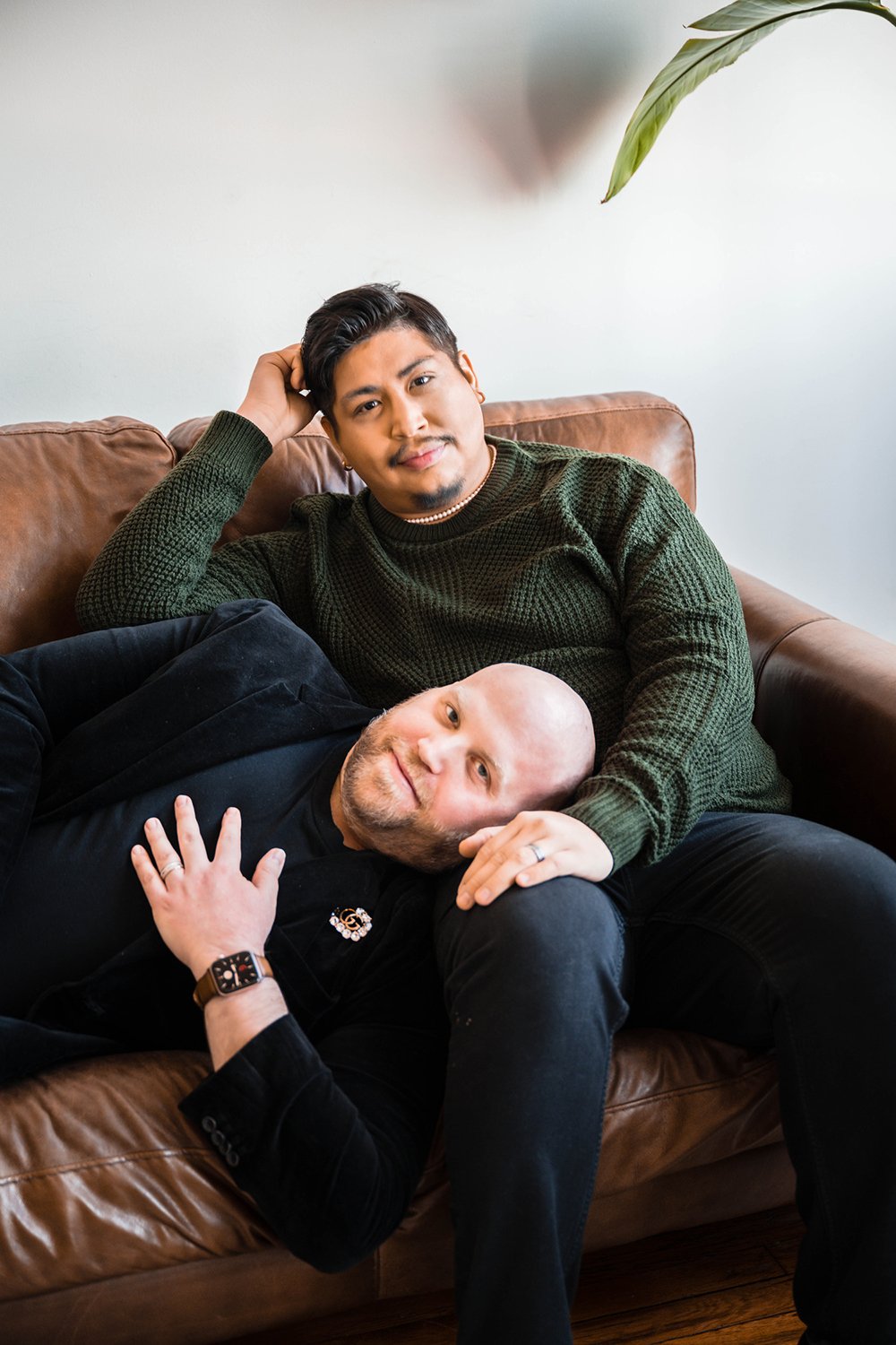 A queer couple sits on the couch for their at-home photoshoot session.