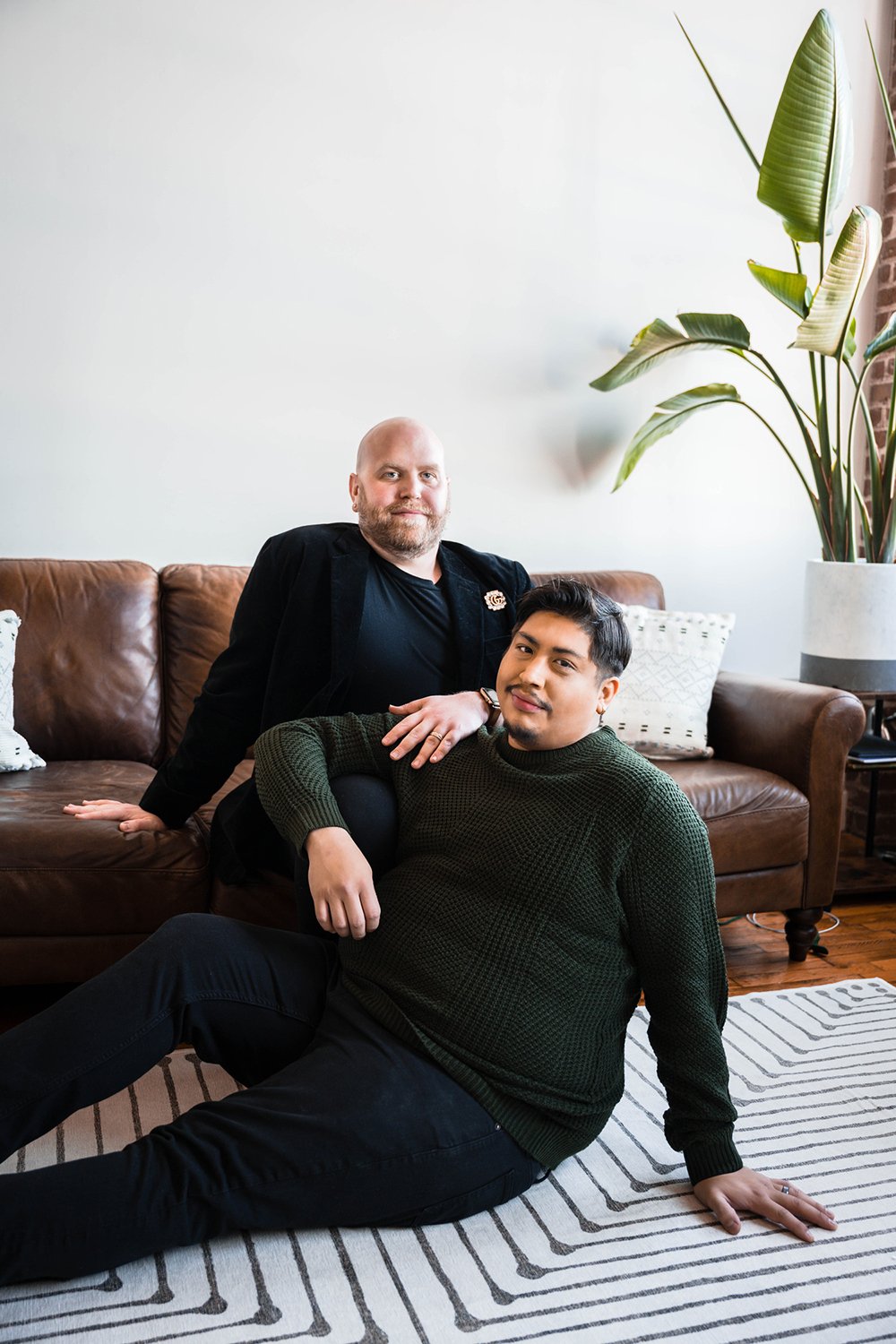 A queer couple sits on the couch in their living room.