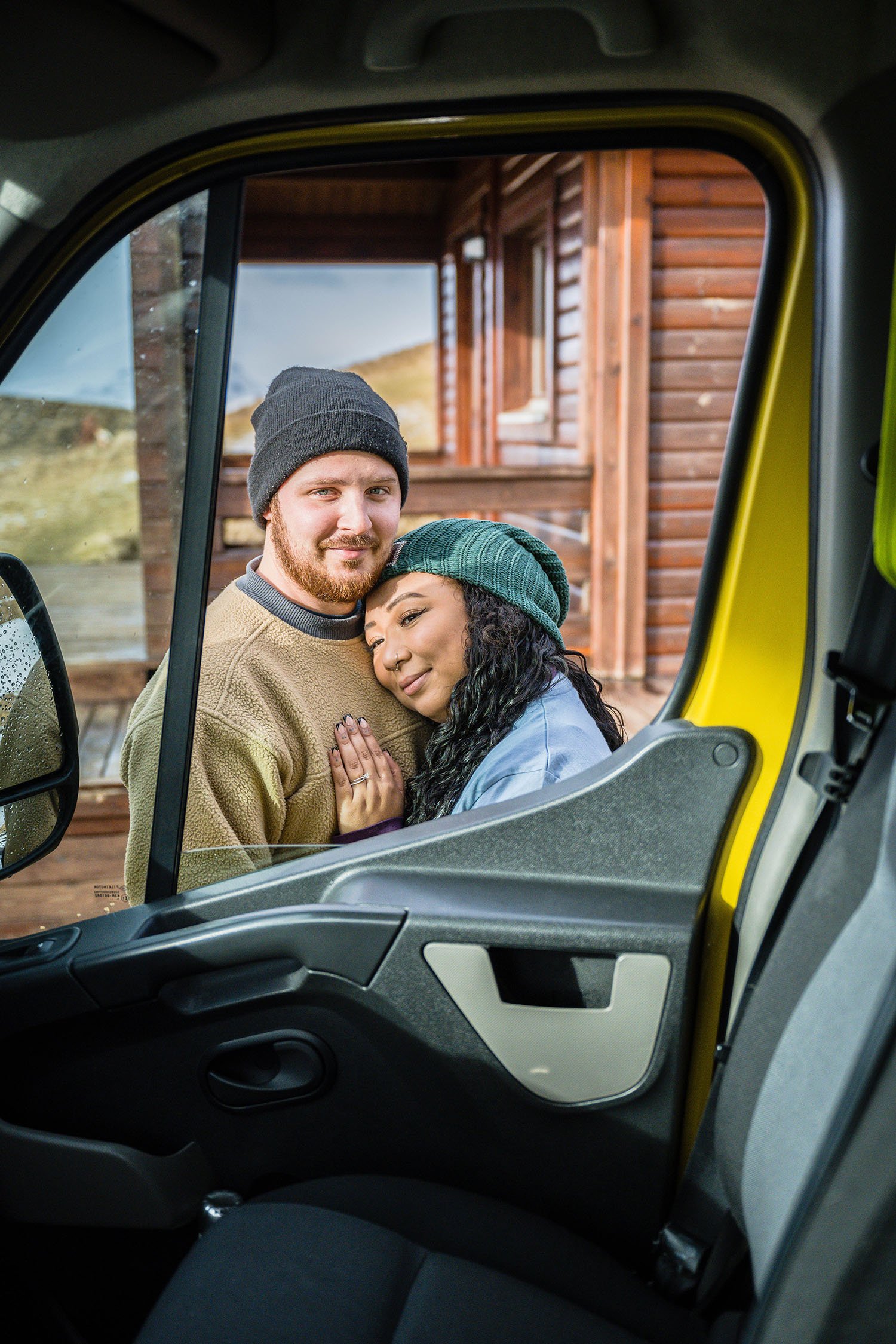 A couple stands outside their campervan and looks through the passenger side window for a photo.