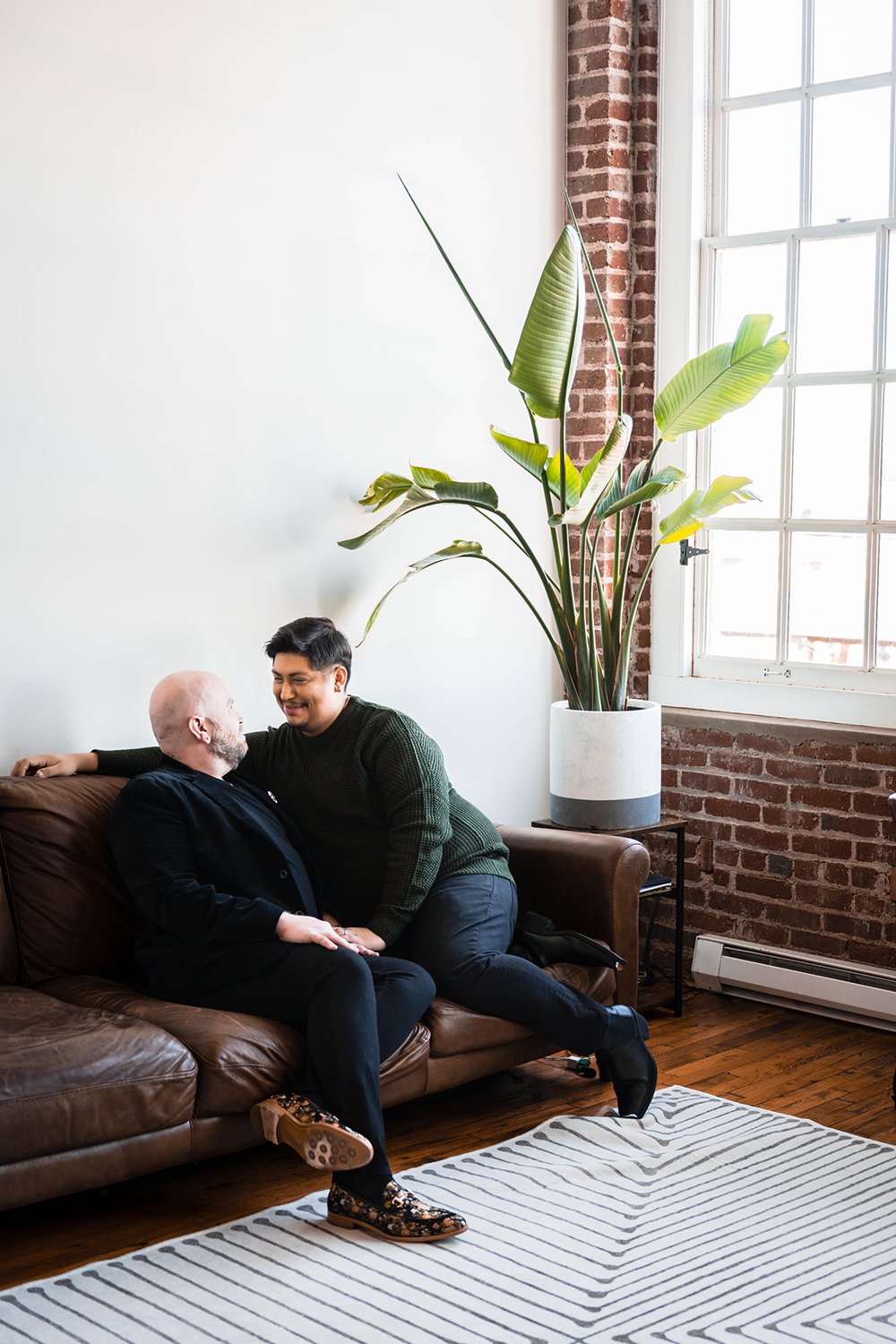 A queer couple sits on the couch in their living room.