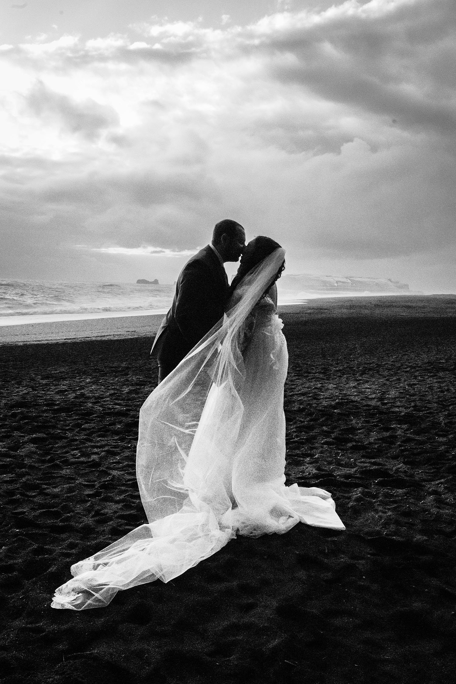 A couple eloping on Reynisfjara Beach in Iceland embrace for their first kiss. 