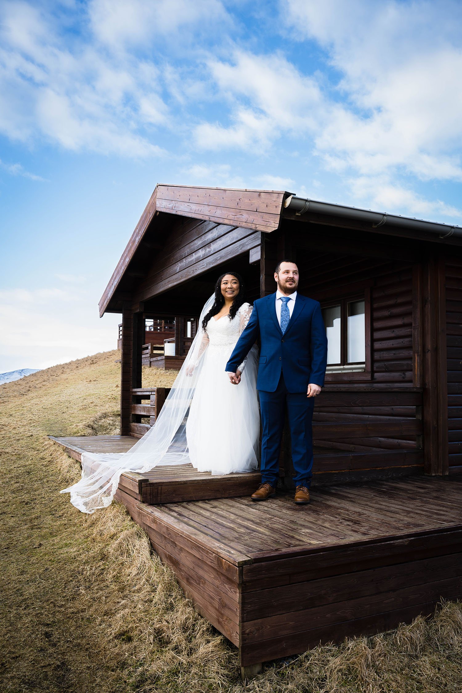 A couple stands outside of their cabin holding hands.