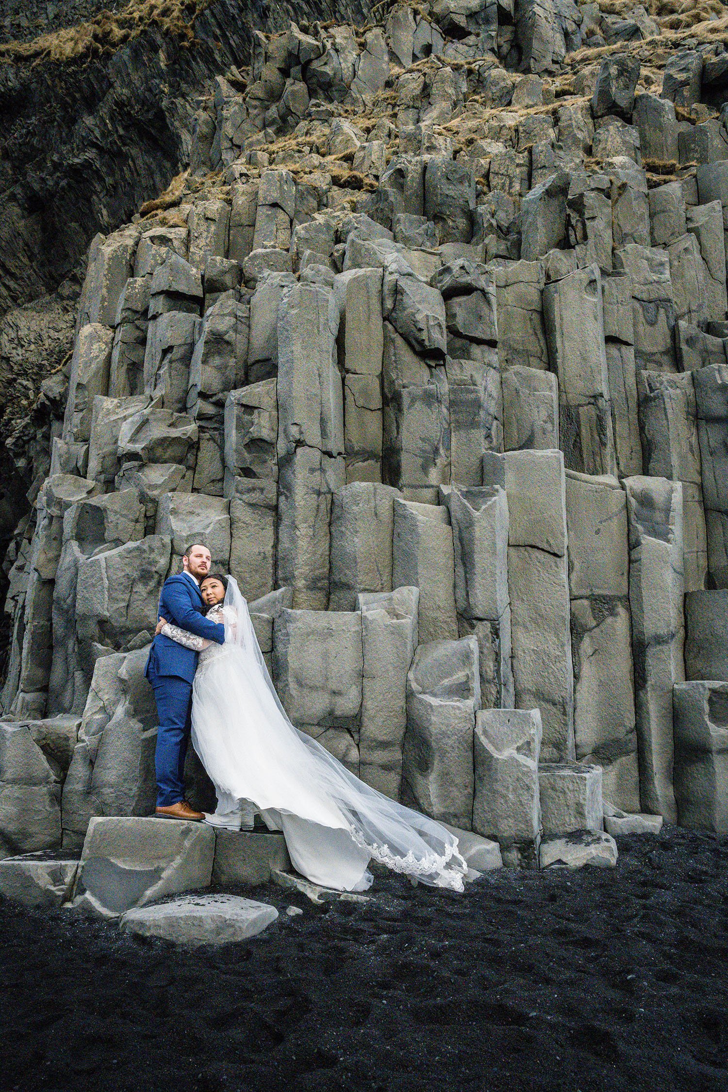 A couple eloping embraces one another while they stand on a basalt column on Reynisfjara Beach, Iceland.