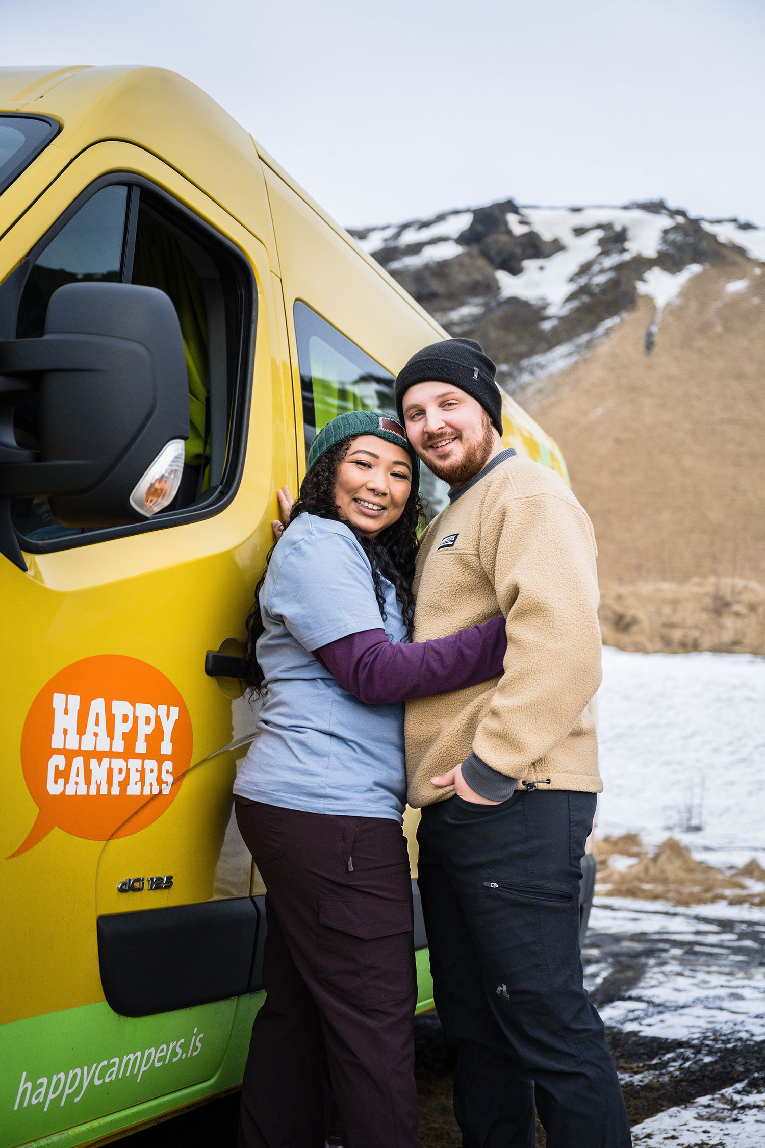 A couple embraces standing next to their Happy Campers campervan.