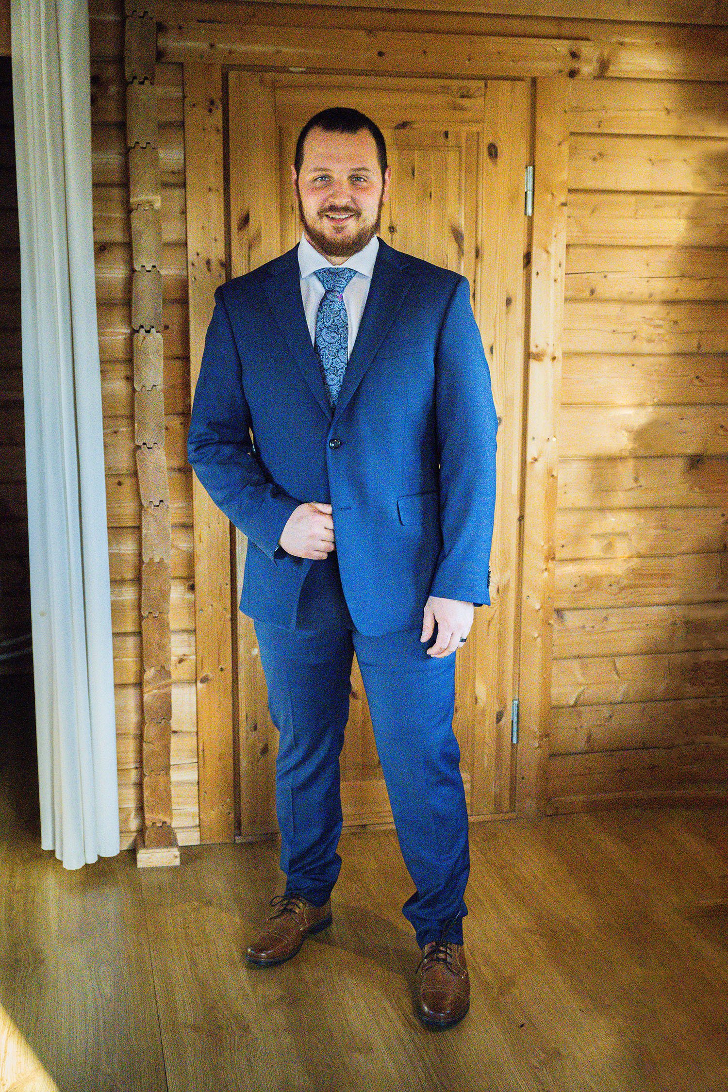 A man wears a blue suit inside of a wooden cabin.