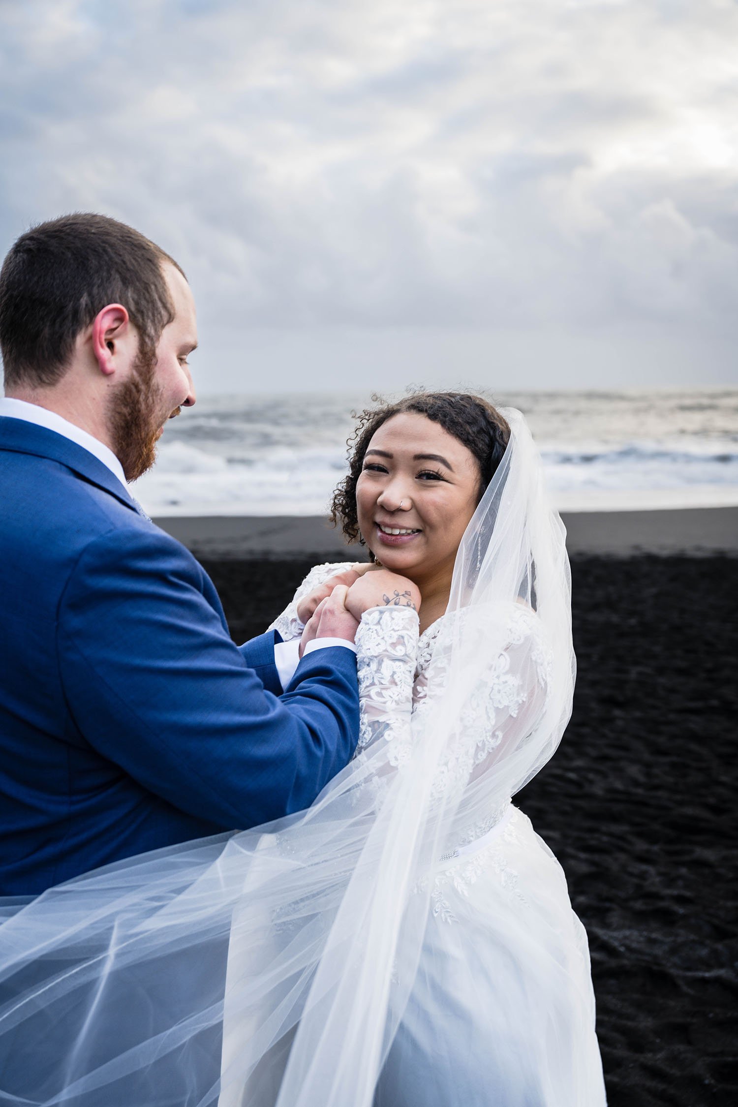 A man holds up a woman's hands towards her chest and the woman smiles towards the camera. 