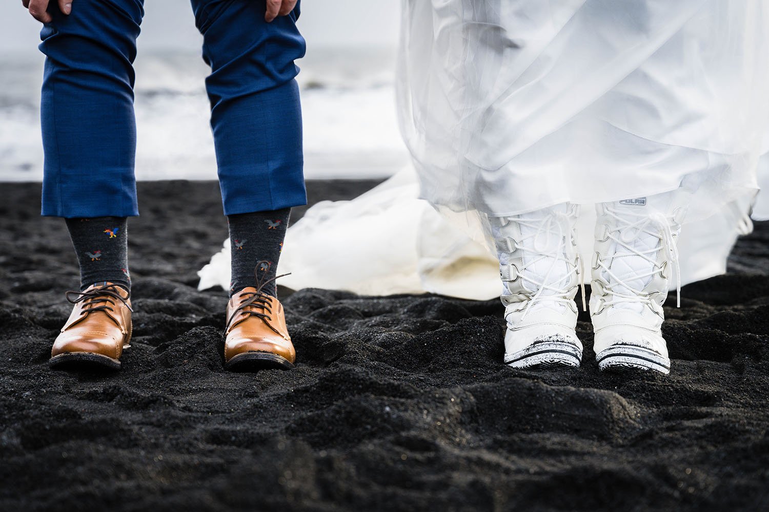 A man lifts his pants to reveal chicken socks and a woman lifts up her dress to reveal her winter boots on Reynisfjara Black Sand Beach in Iceland.