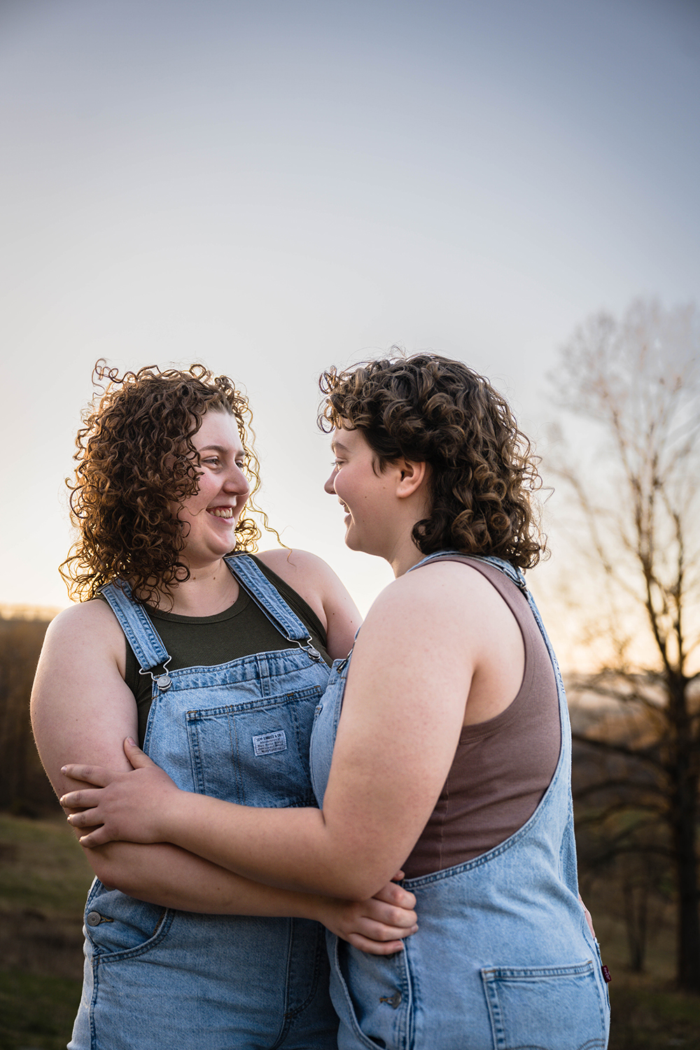 An LGBTQ+ couple smiles widely at one another as they hug during their anniversary portrait session in Southwest Virginia.