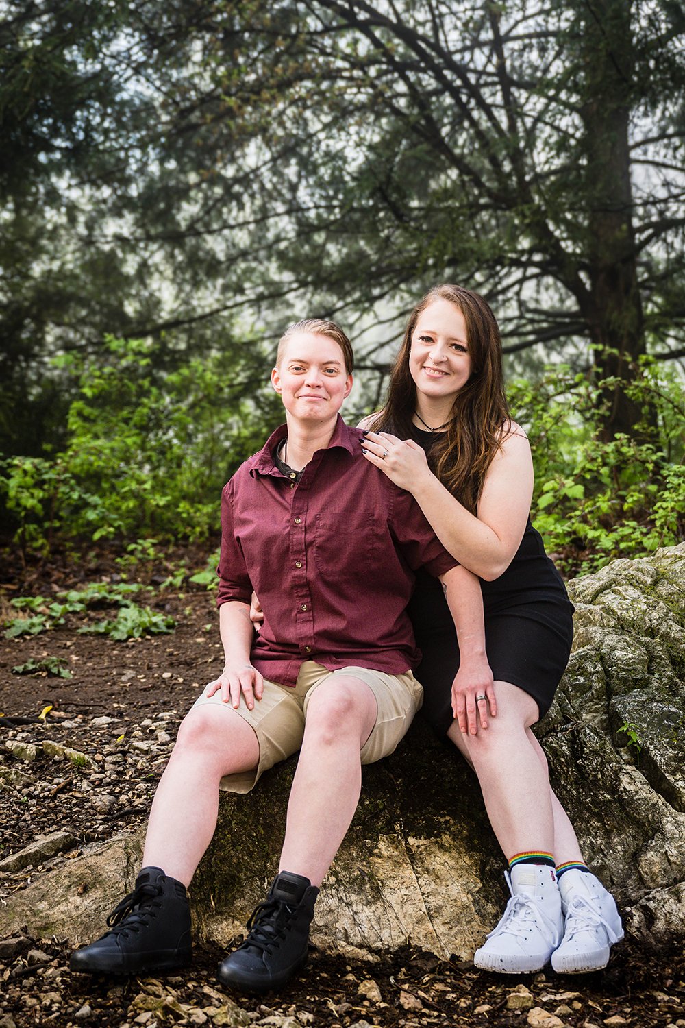 An lgbtq+ couple sits on a large rock located at the summit of Mill Mountain for their Roanoke Star engagement session in Virginia.