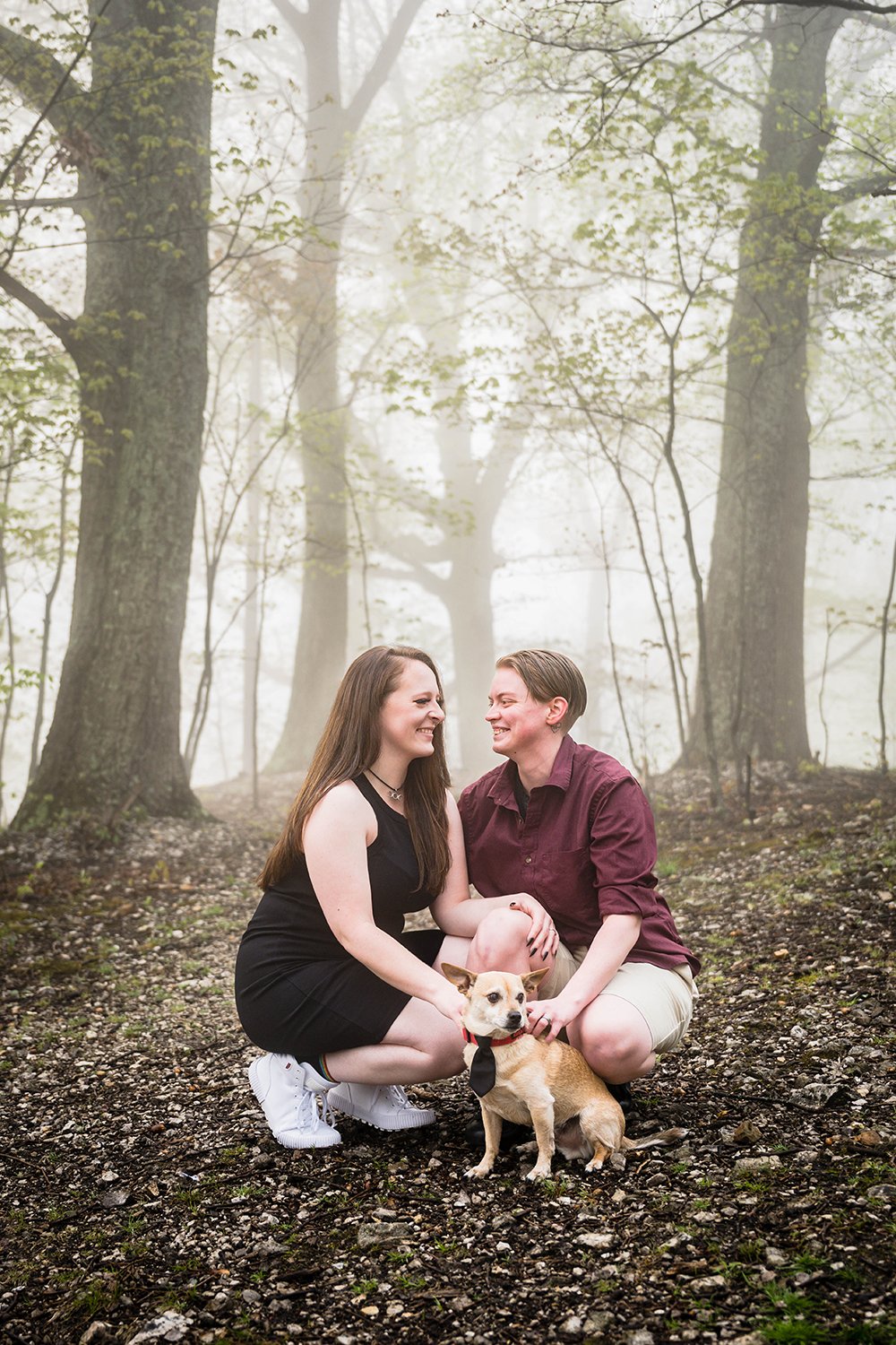 A Virginia lgbtq+ couple smile at one another and hold onto their dog for Roanoke Star engagement session.