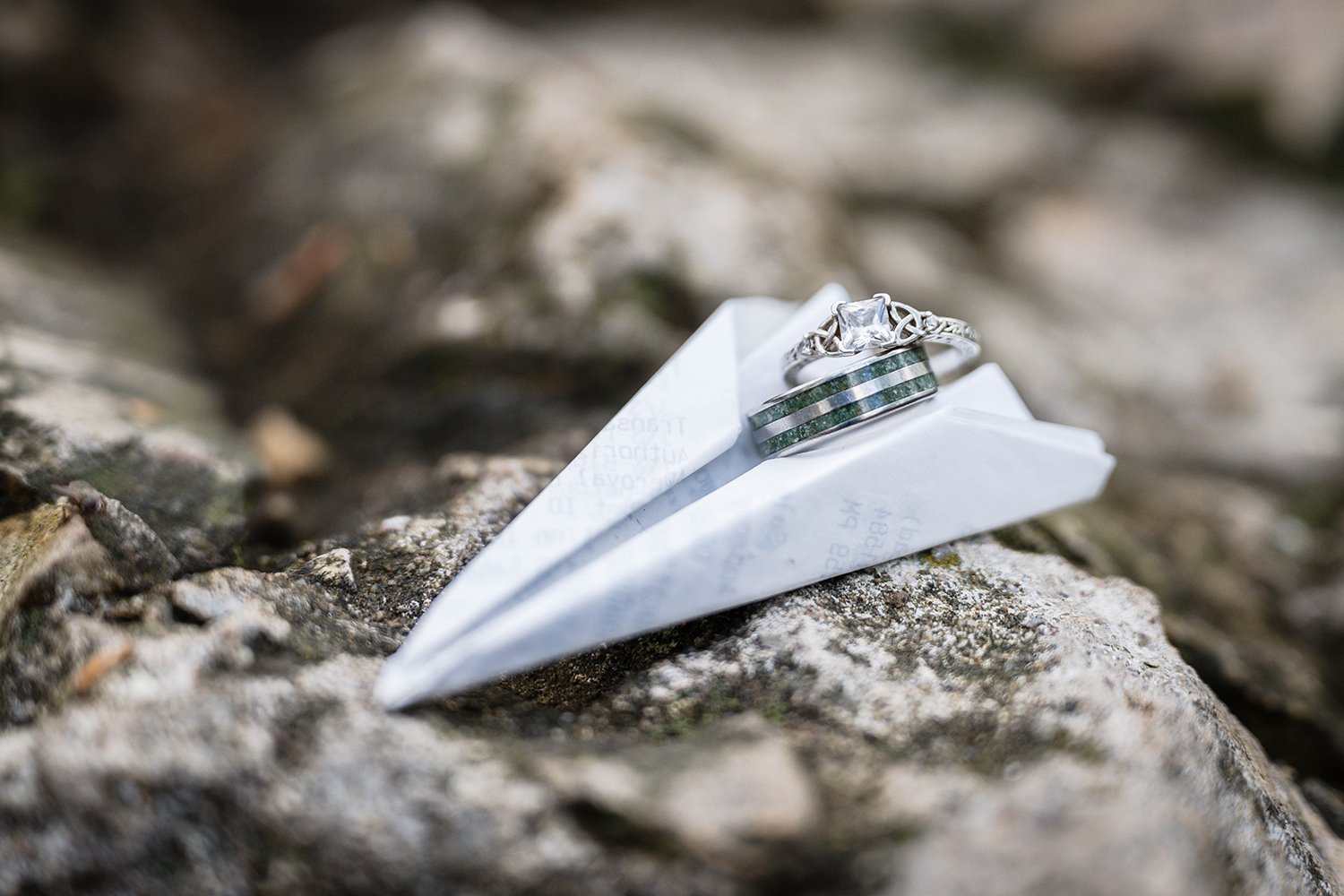 A pair of engagement rings sit inside the crevice of a paper airplane atop a rock for a couple's engagement session at Mill Mountain in Virginia.